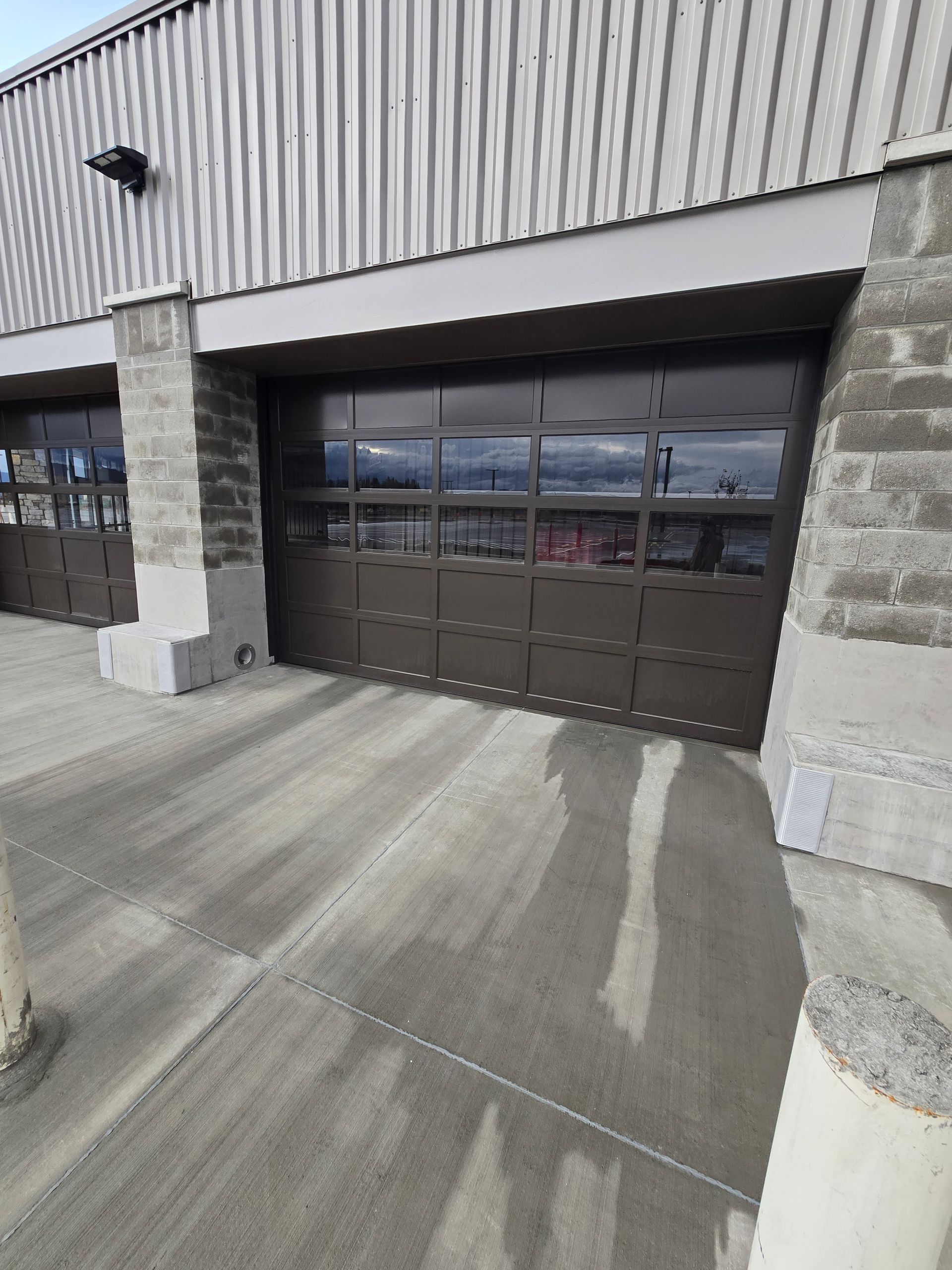 A commercial building with dark brown, multi-paneled glass garage doors and a corrugated metal facade.