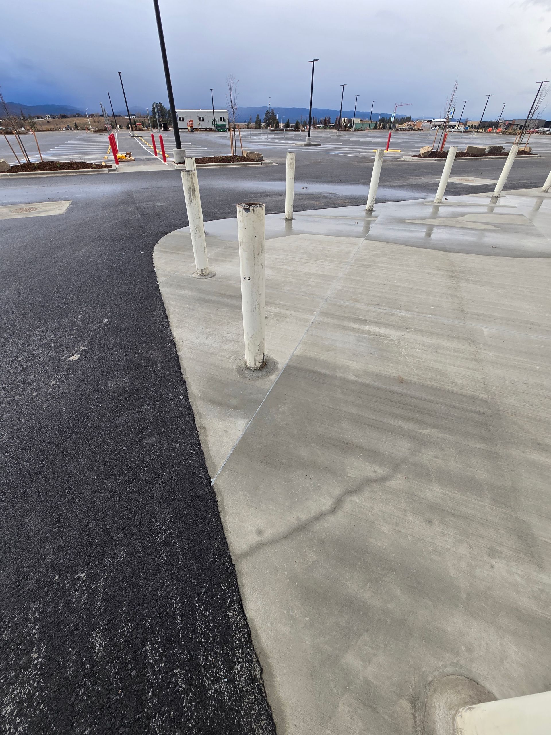 A row of white bollards on a concrete sidewalk bordering an asphalt parking lot under a cloudy sky.