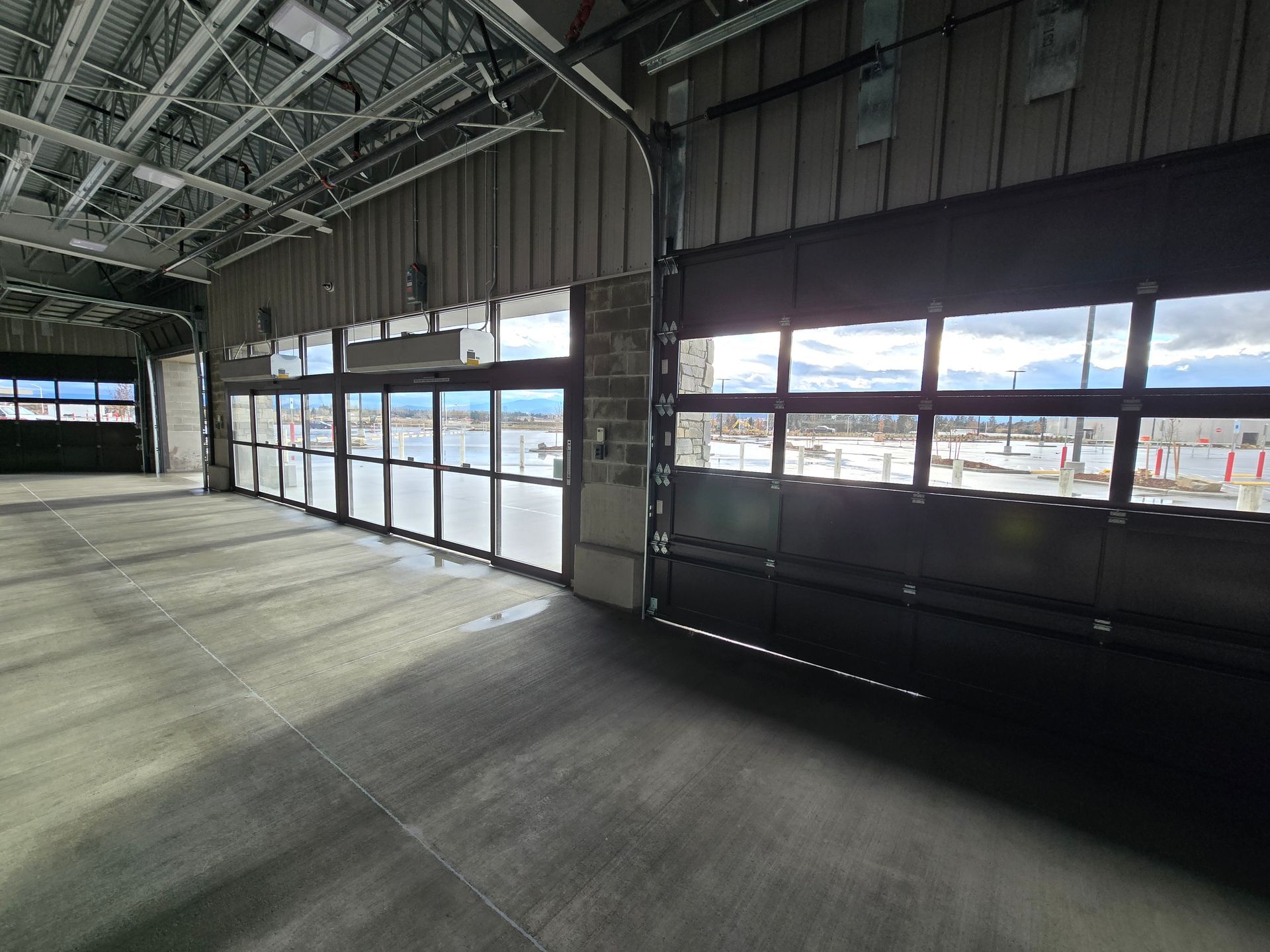 An expansive, empty industrial bay with large glass roll-up garage doors looking out onto a snowy, overcast landscape.