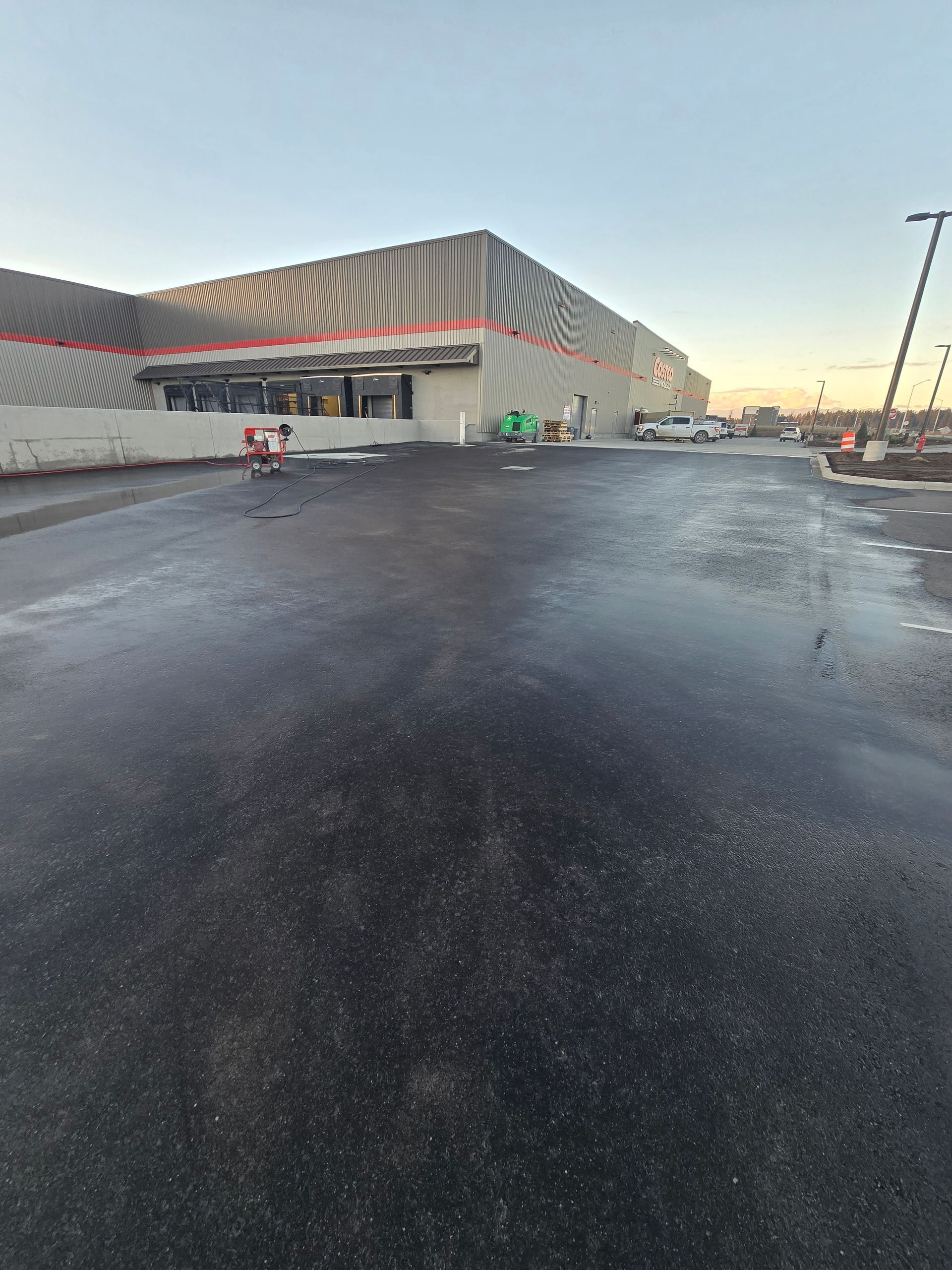 A large, modern warehouse-style building with patterned gray and white metal siding stands above a freshly paved asphalt lot.