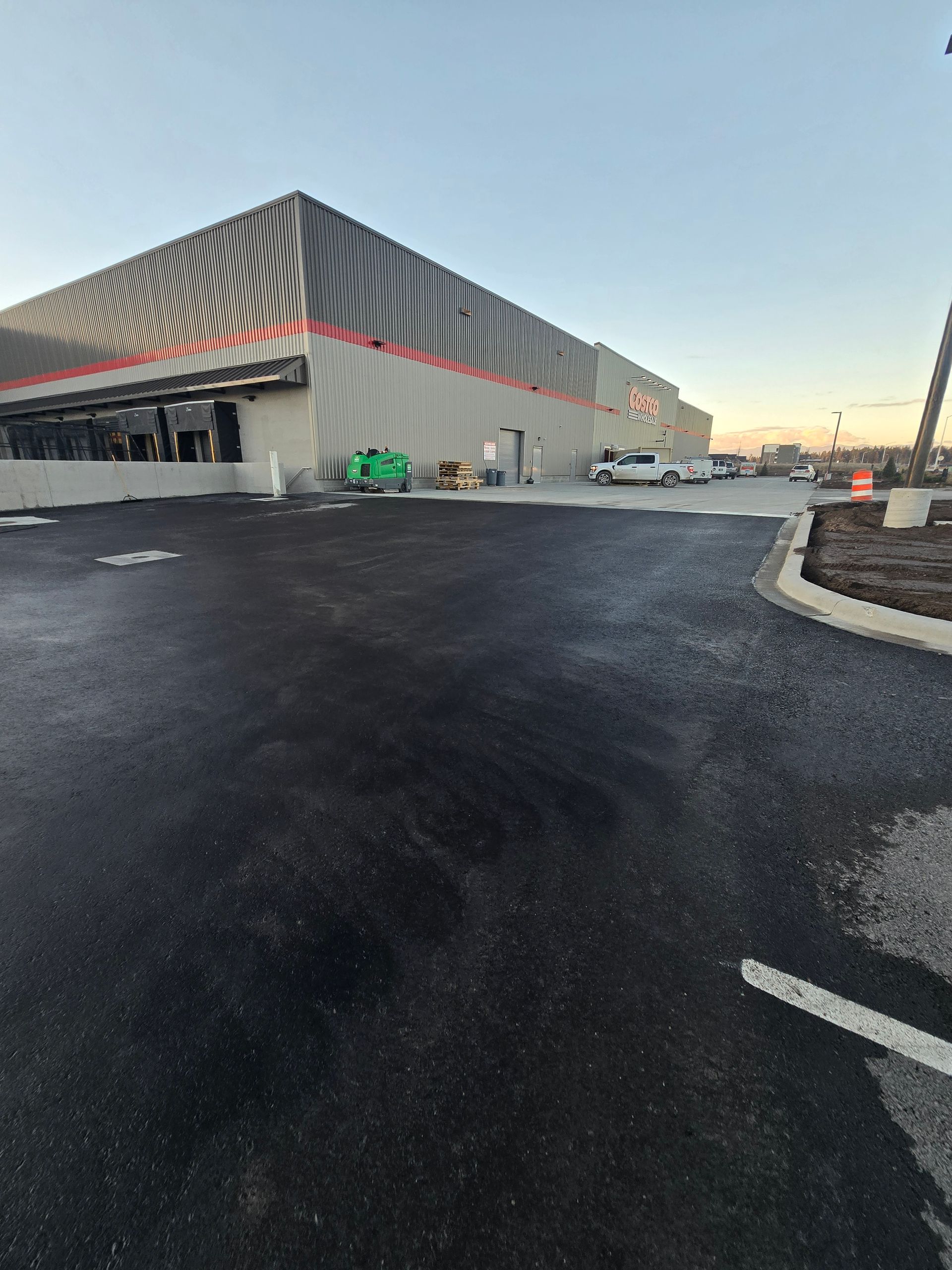A large warehouse building with striped gray siding and orange accents, set against a paved lot at sunset.
