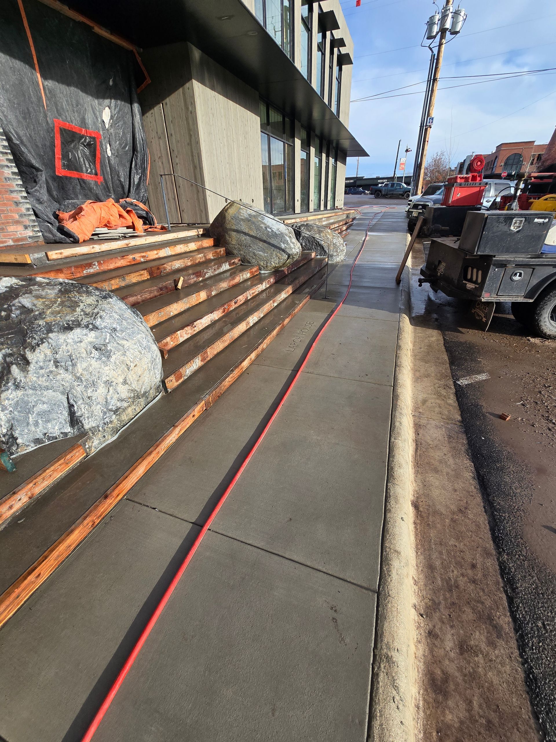 Large boulders block a set of concrete steps leading to a building entrance next to a sidewalk.