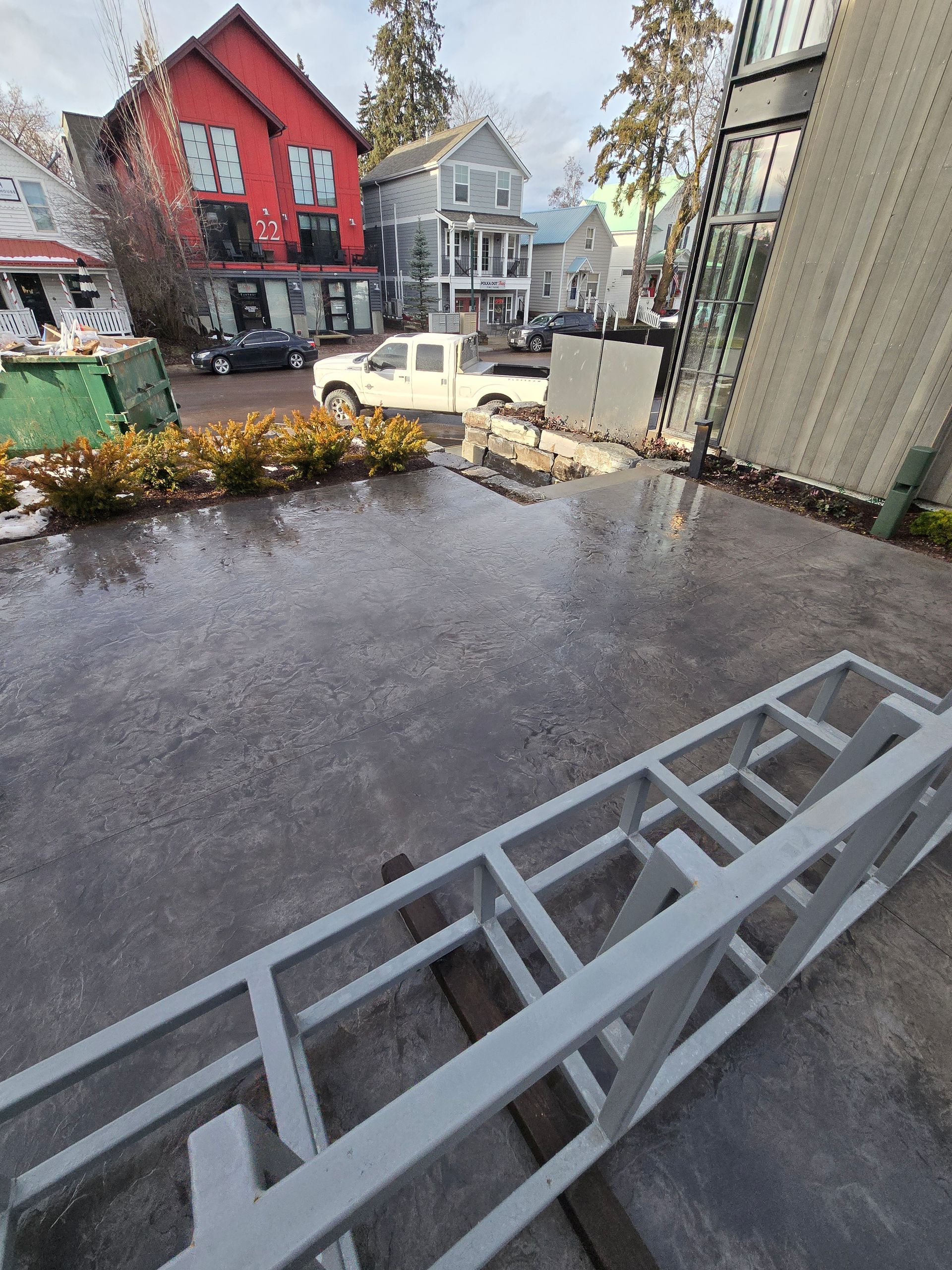 A gray metal frame sits on a wet patio, overlooking a street with a red building and a white truck.
