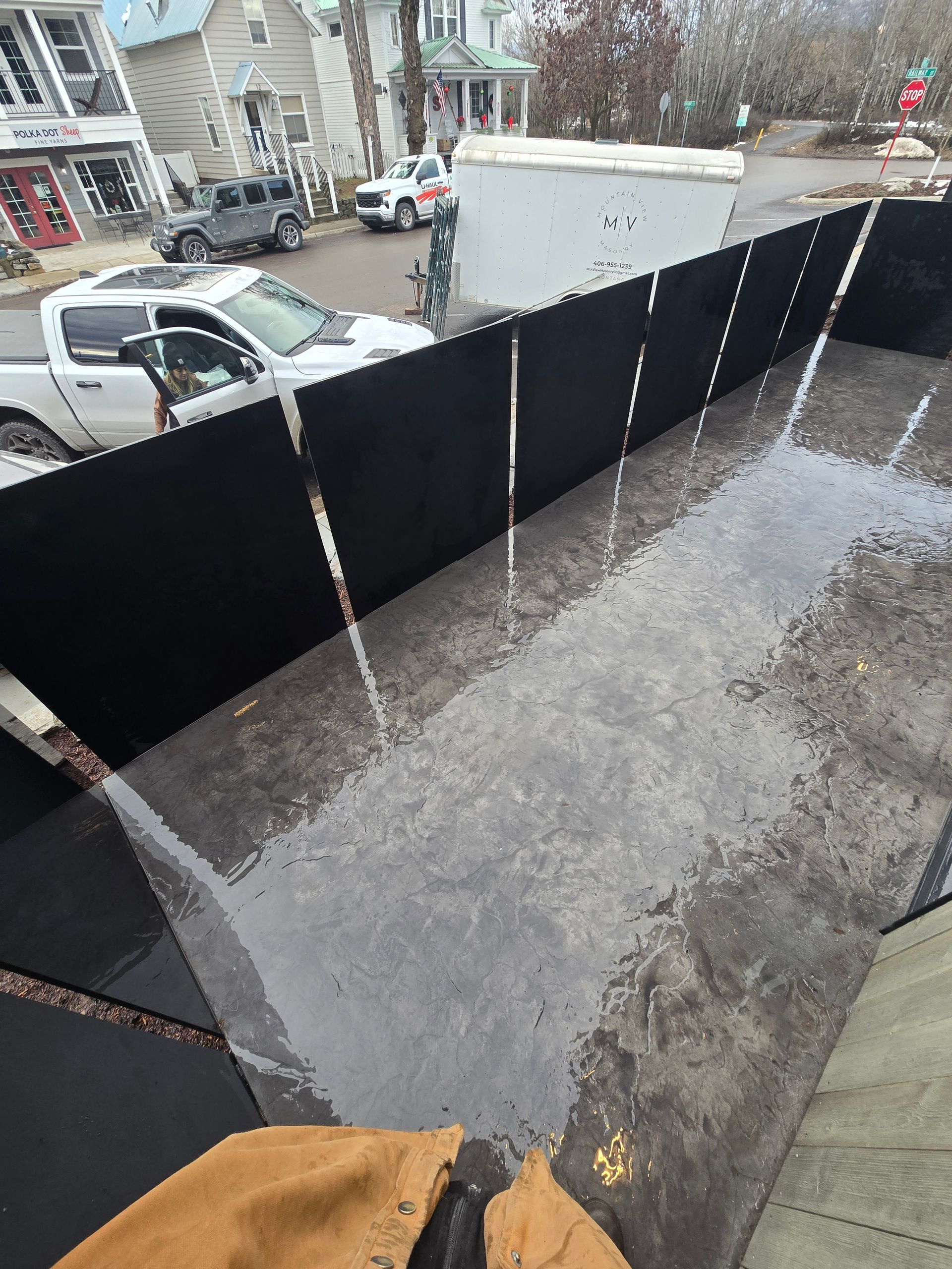 A high-angle view of a patio area enclosed by a black privacy screen, with a parked pickup truck visible in the background.