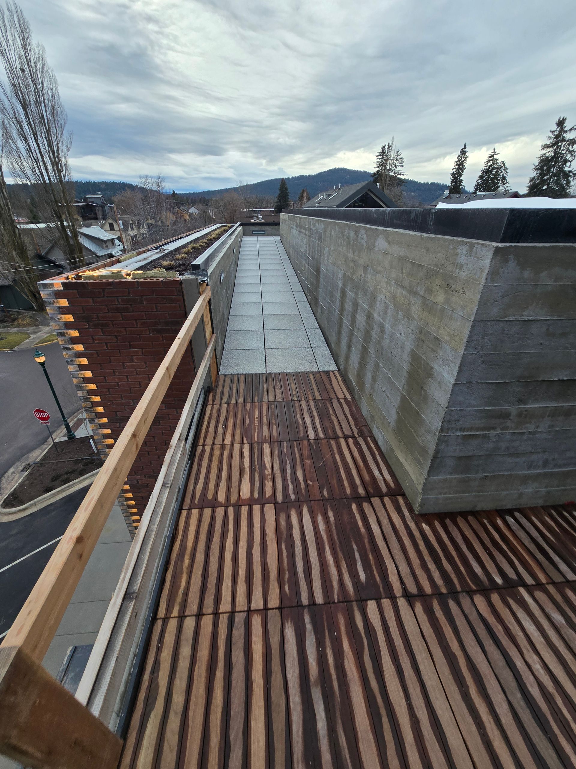 A high-angle view of a wooden walkway and a concrete path alongside a modern building structure under a cloudy sky.