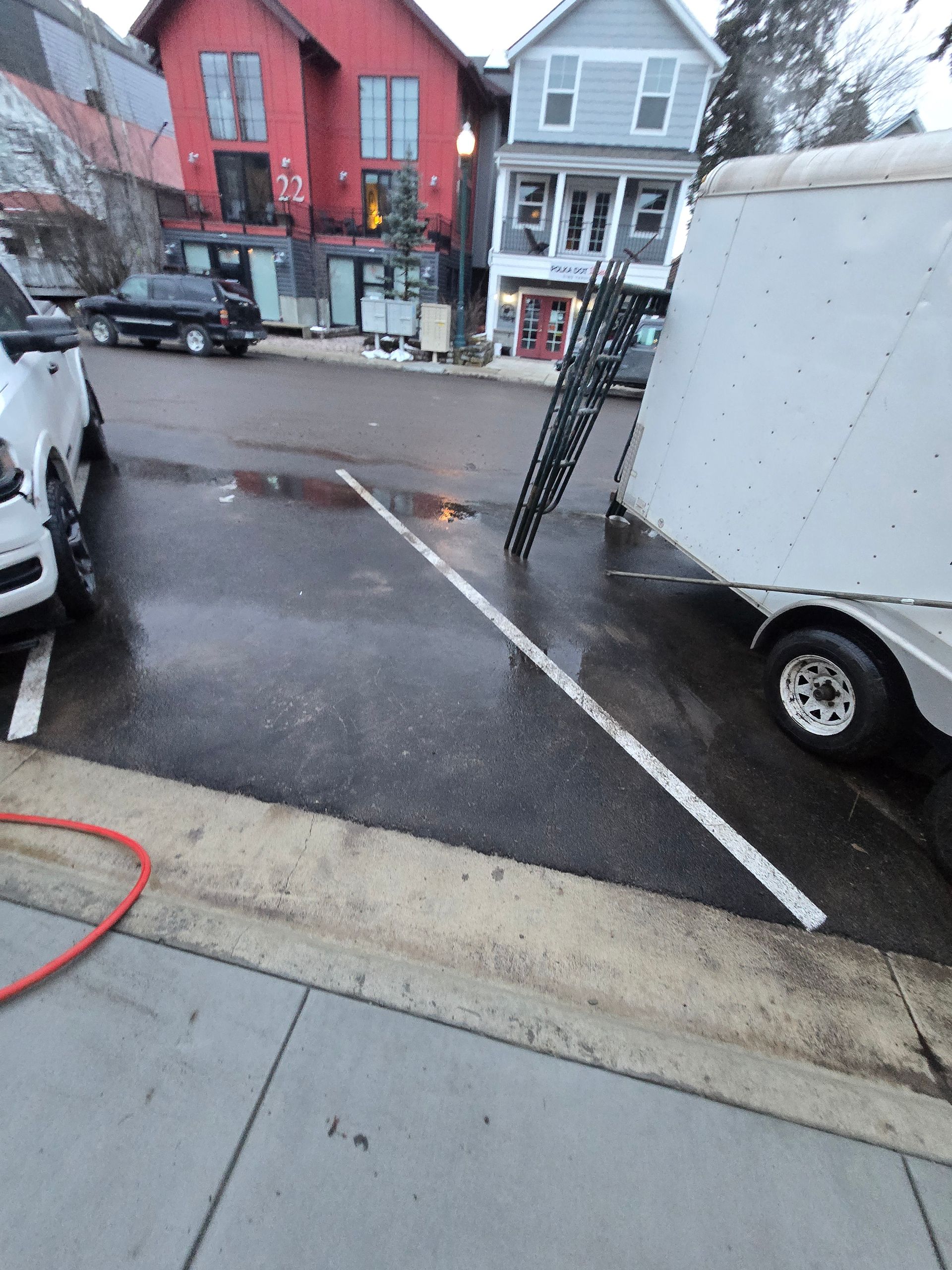 A white utility trailer parked in a street-side parking space next to a black metal ramp and a car.