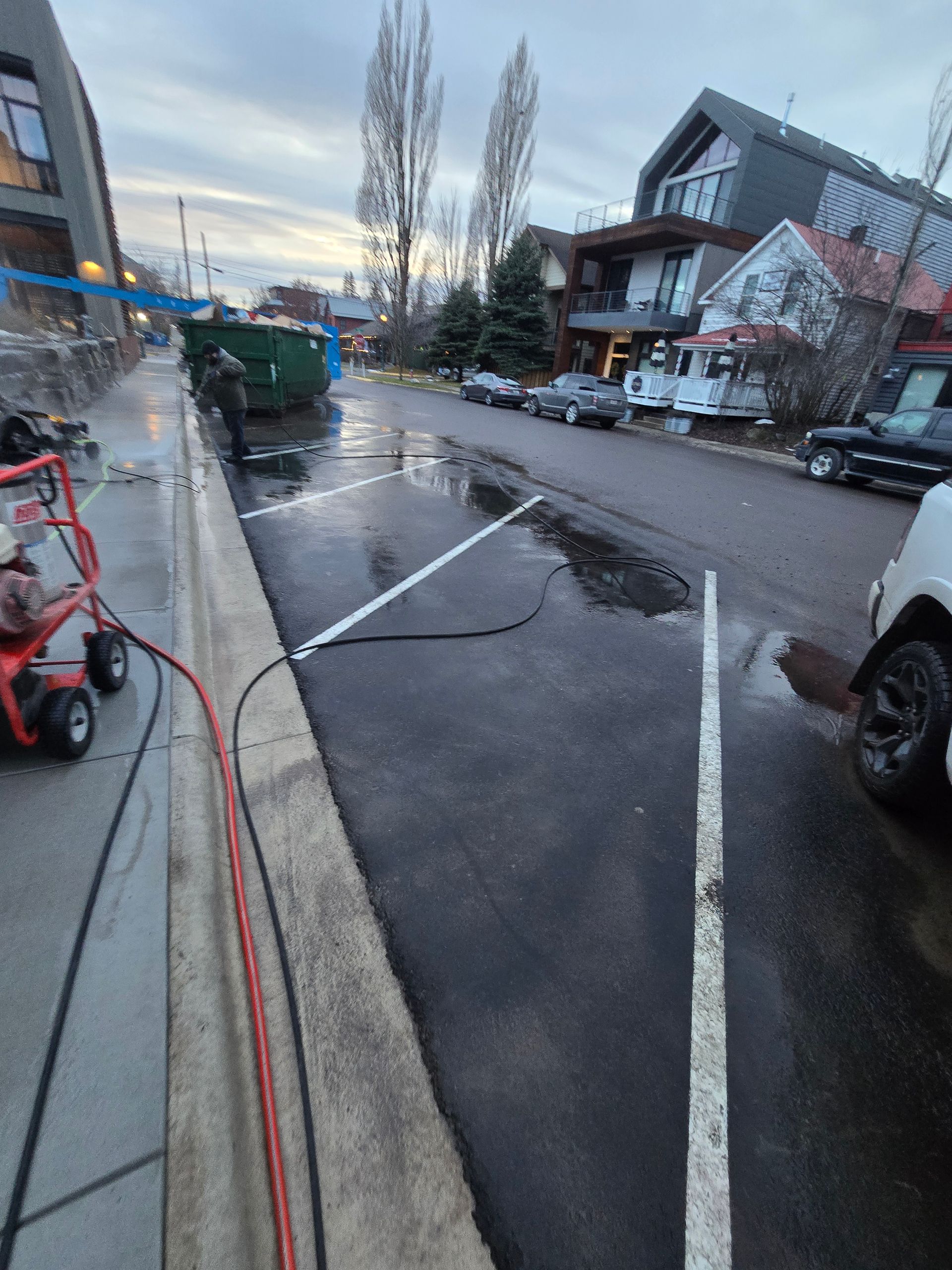 An outdoor scene shows a street with parking spaces, a green dumpster, and an industrial cleaner with hoses on the left.