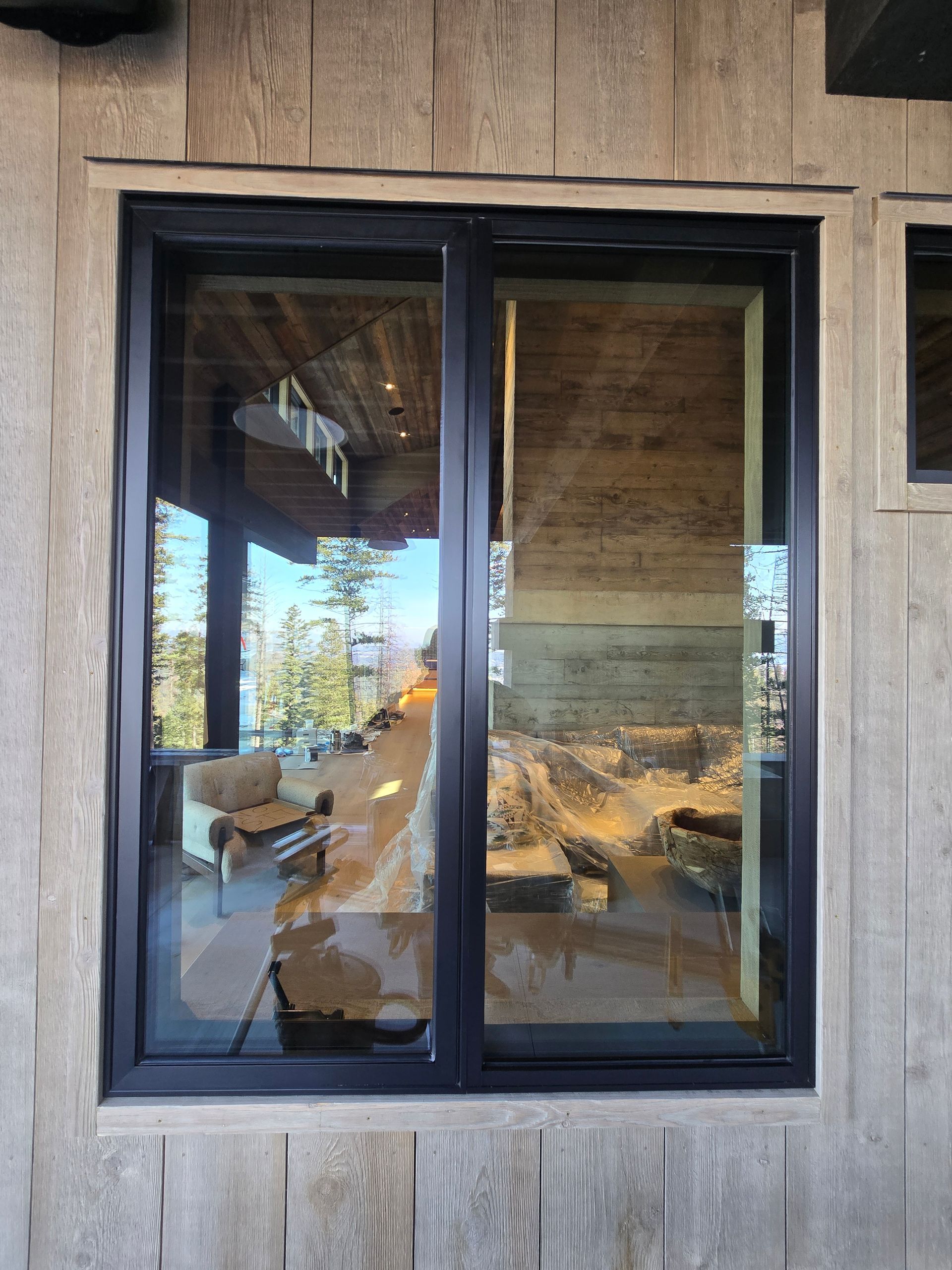 A black-framed, rectangular window set into a light-colored, vertical-planked wooden wall, reflecting an indoor lounge.