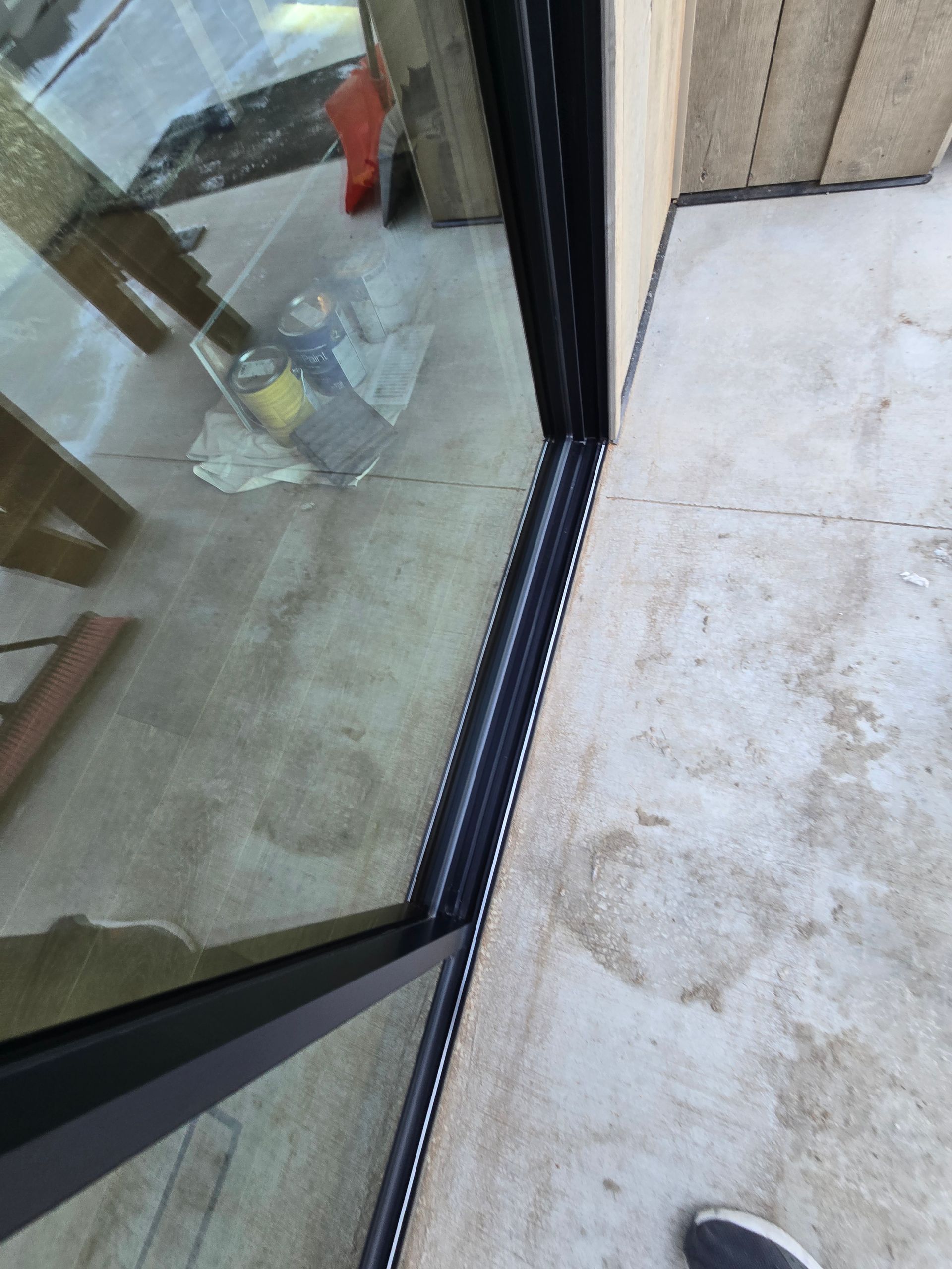 A close-up view of the black metal frame of a sliding glass door installed on a concrete patio.