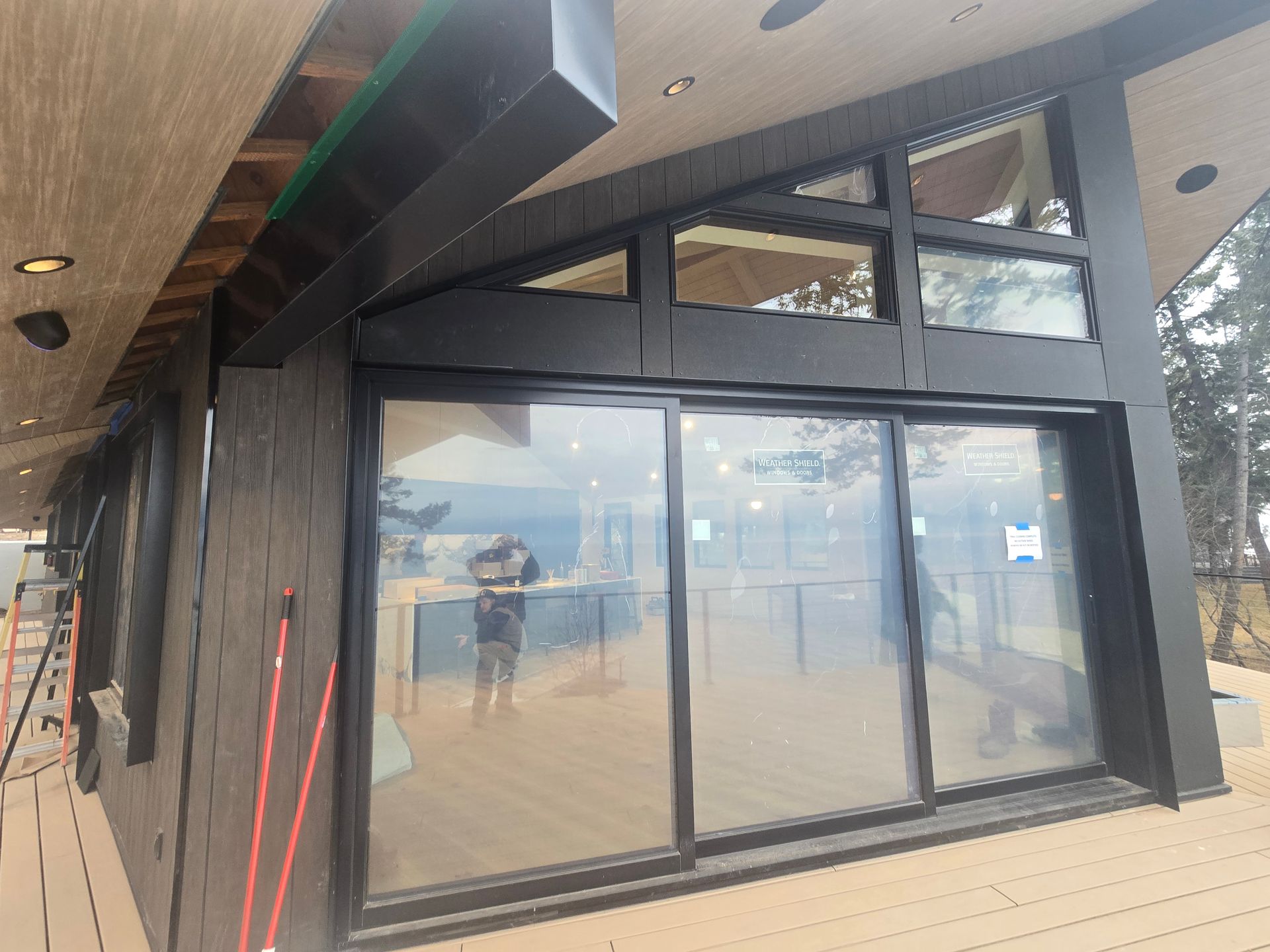 A modern building exterior featuring dark wood siding, black-framed sliding glass doors, and clerestory windows on a deck.