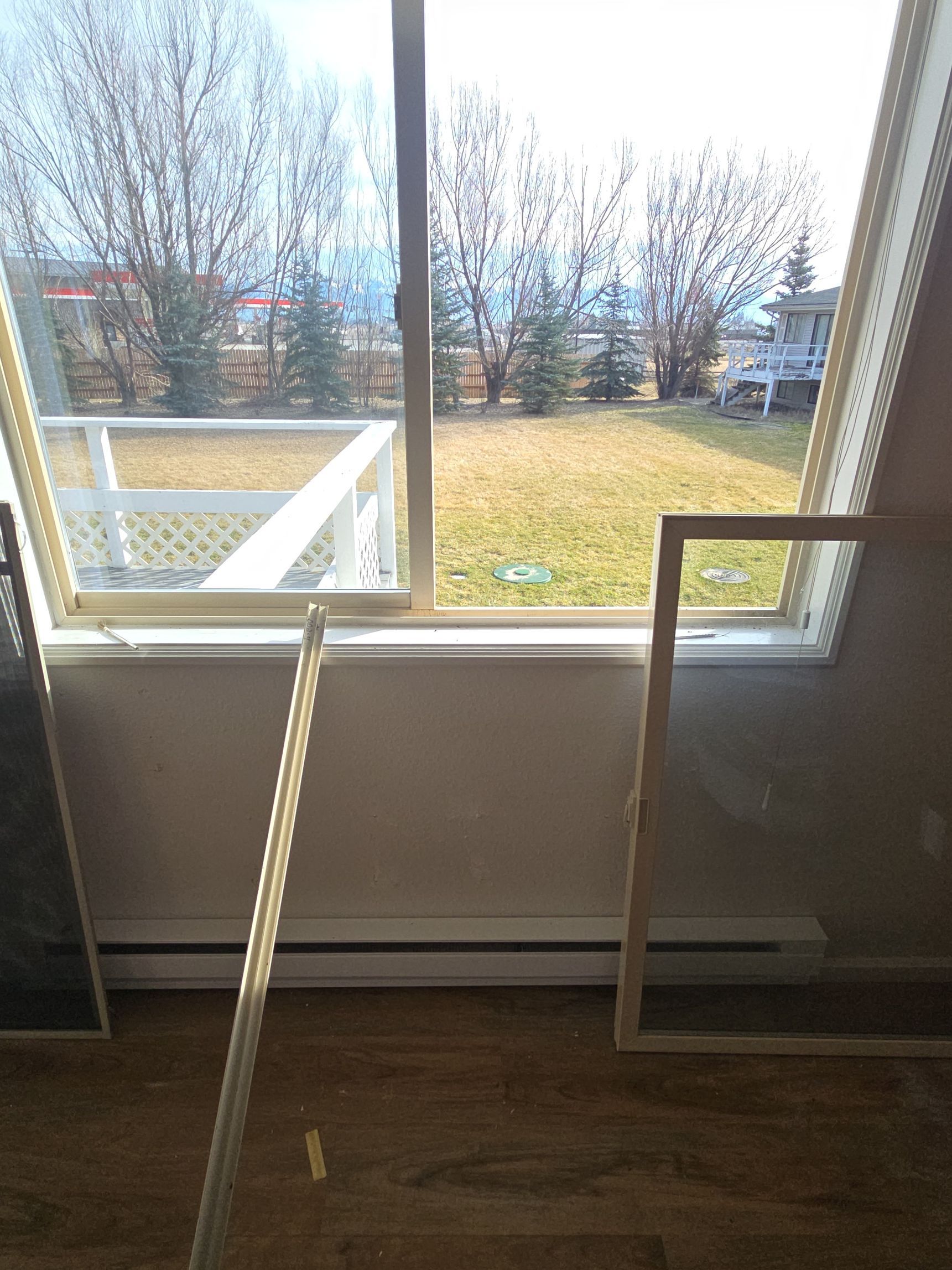 A window with a removed screen leaning nearby, with a view of a backyard deck and trees beyond.