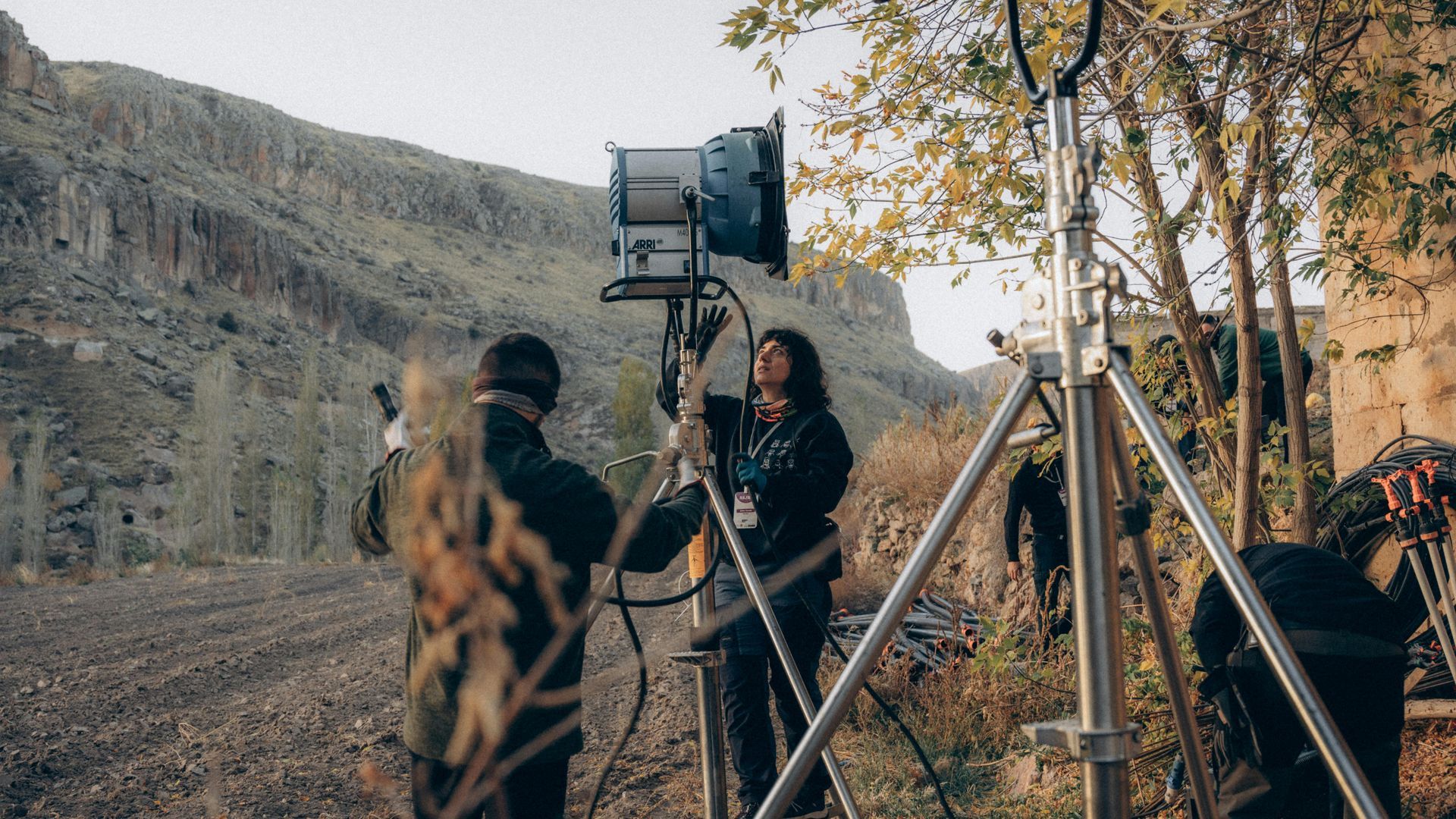 Film crew filming outdoors in a rocky valley with a camera on a tripod and lights setup