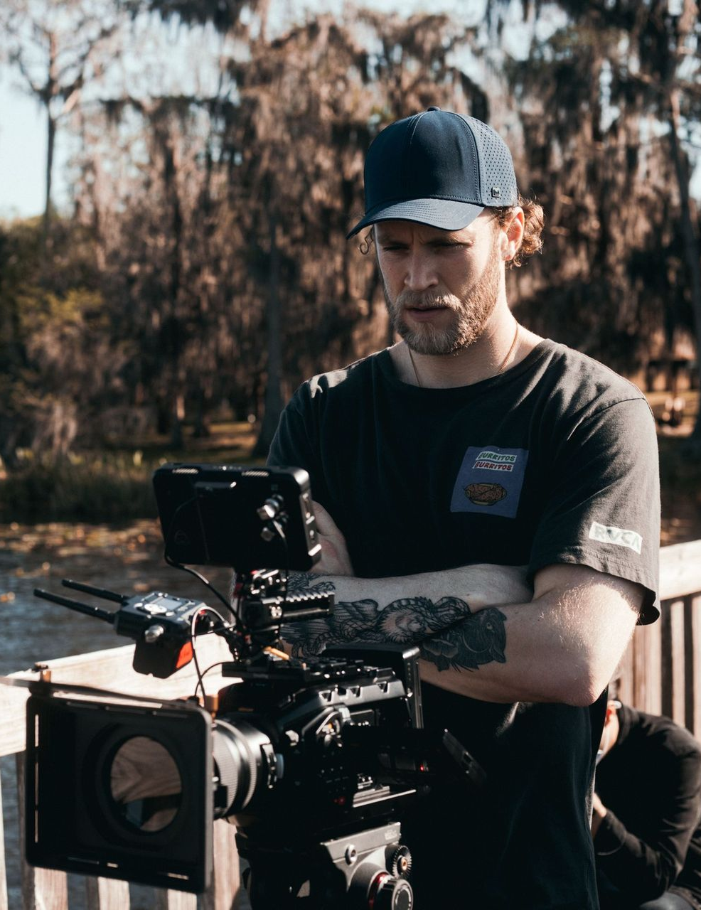 Person operating a professional camera outdoors in a black cap and shirt.