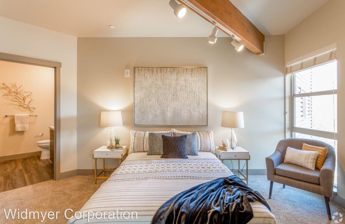 A bedroom with a large bed , chair , lamps and a bathroom.