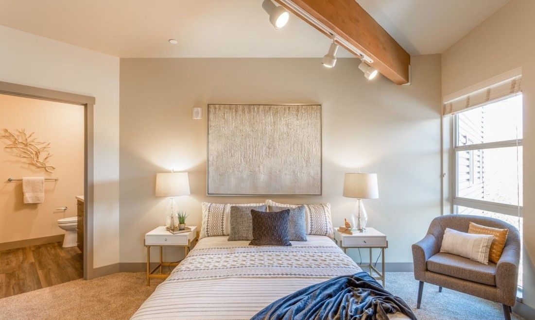 A bedroom with a bed , chair , nightstand and a painting on the wall.