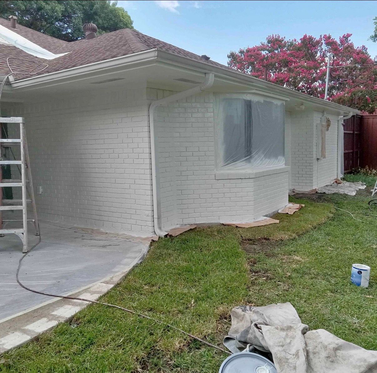 House exterior partially painted white, with a ladder and paint cans present.