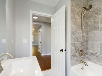 Bathroom interior with a white sink, open door to a hallway, and a tiled shower area.