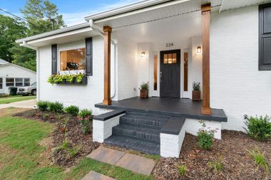 White brick house with dark door, wooden columns, and steps leading to the front porch.