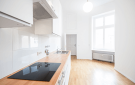 Bright, minimalist kitchen with wooden countertop, black stovetop, white cabinets, and large window.