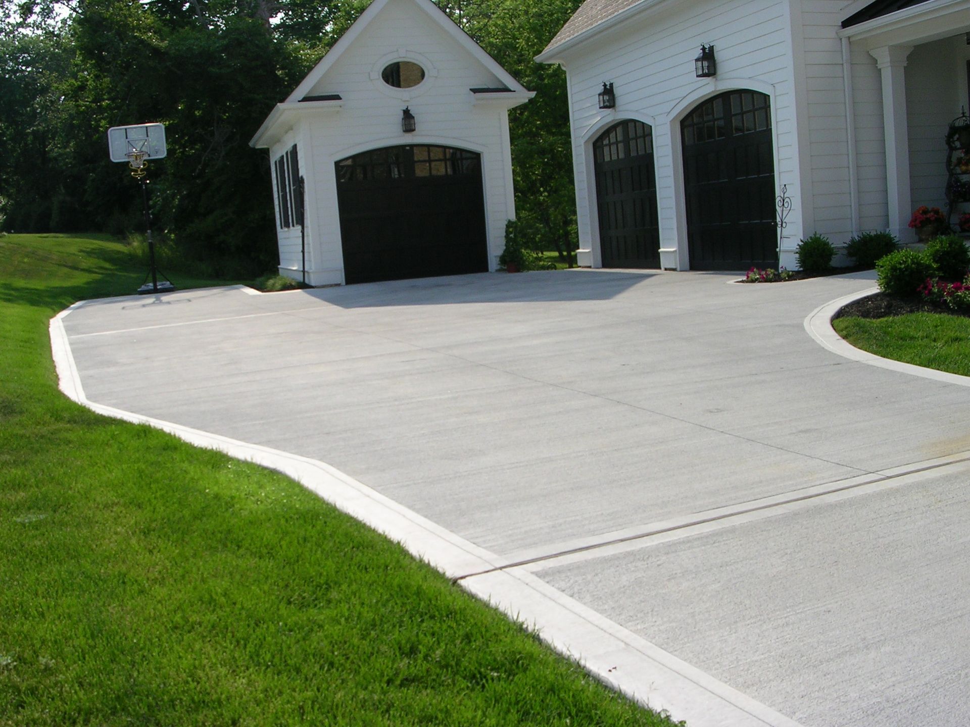 A concrete driveway leading to a white house with black garage doors