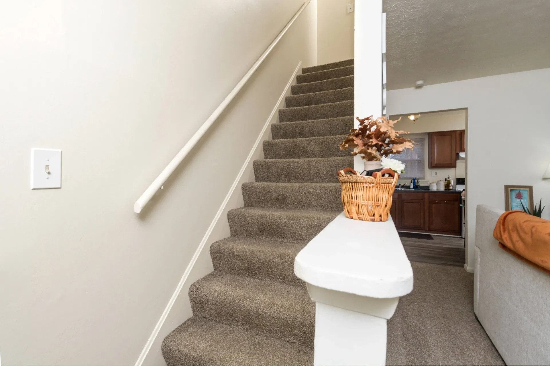 Staircase with carpeted steps, white railing, and decorative basket atop a column, leading upward.