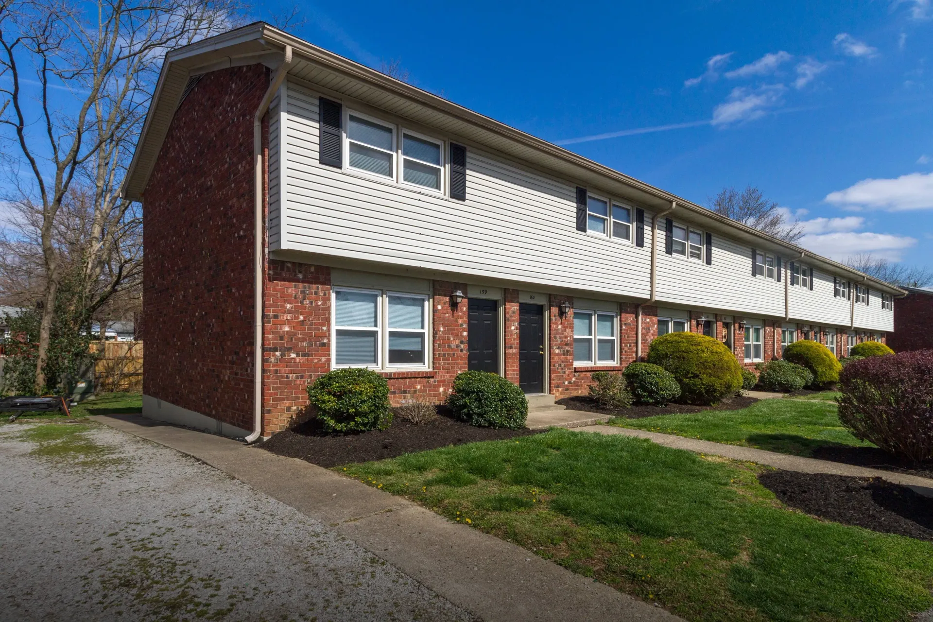 Row of brick townhouses with white siding and black doors, on a sunny day.