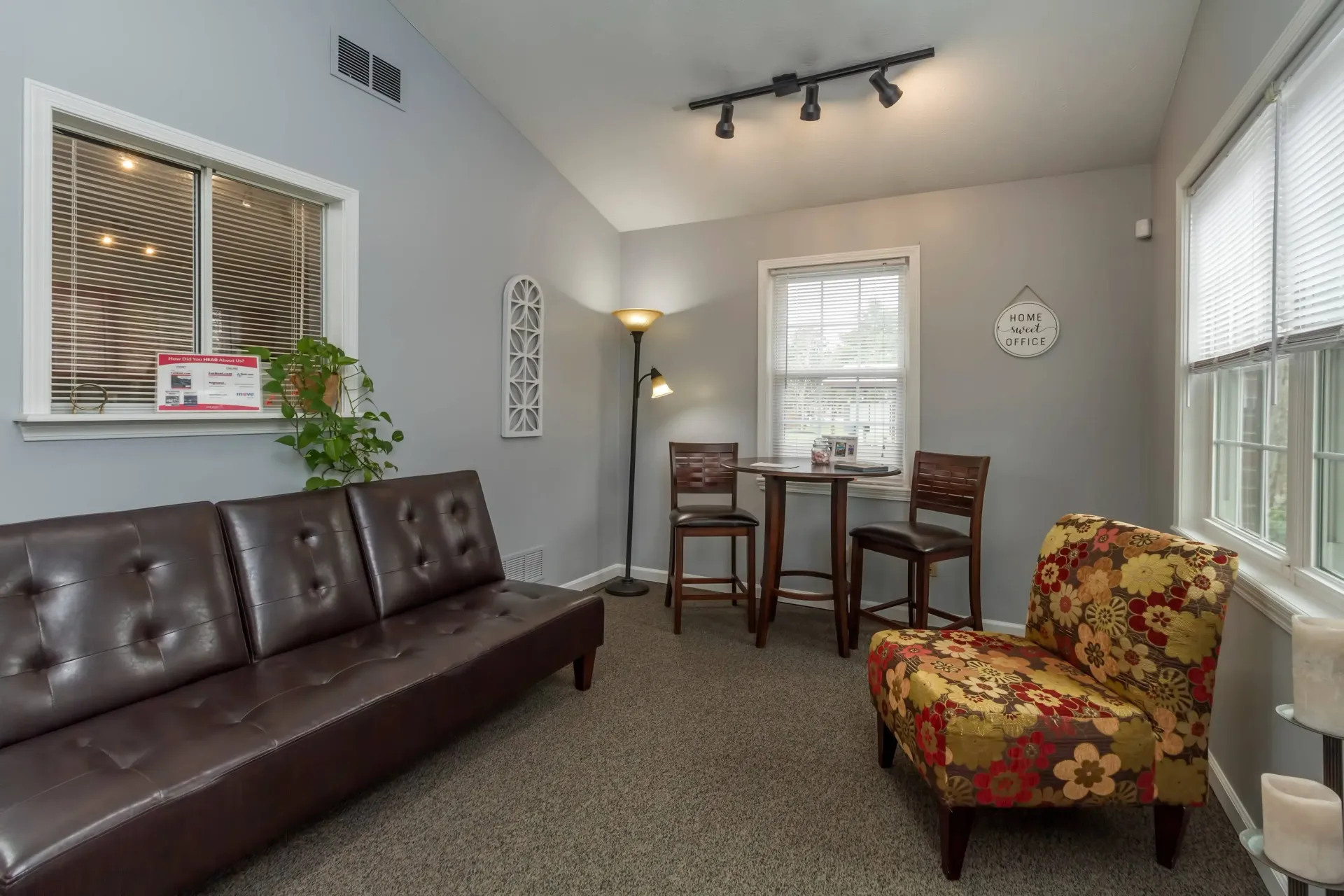 Living room with brown leather sofa, floral armchair, small table, and neutral walls.