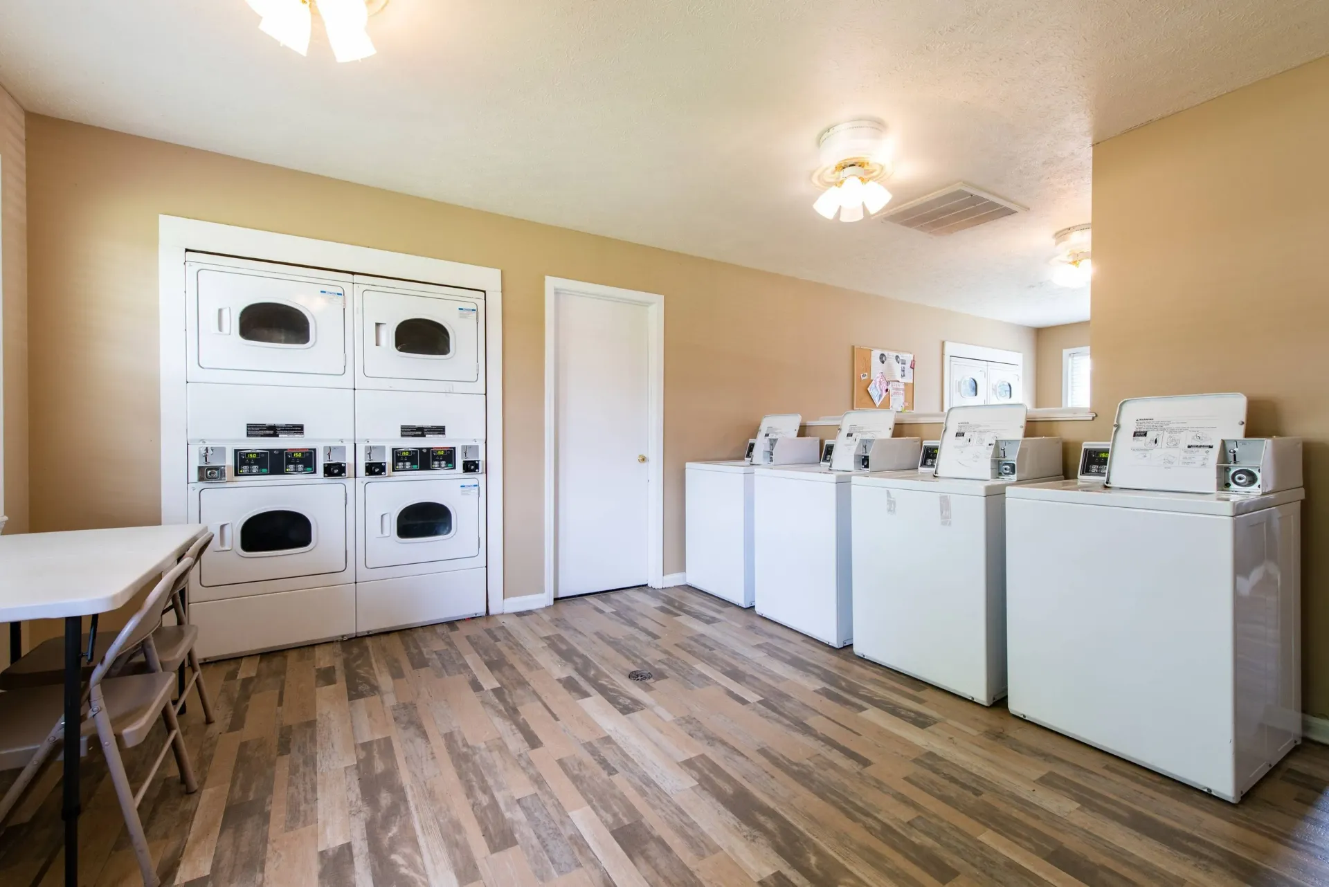 Laundry room with dryers, washers, folding table, and wooden floors.
