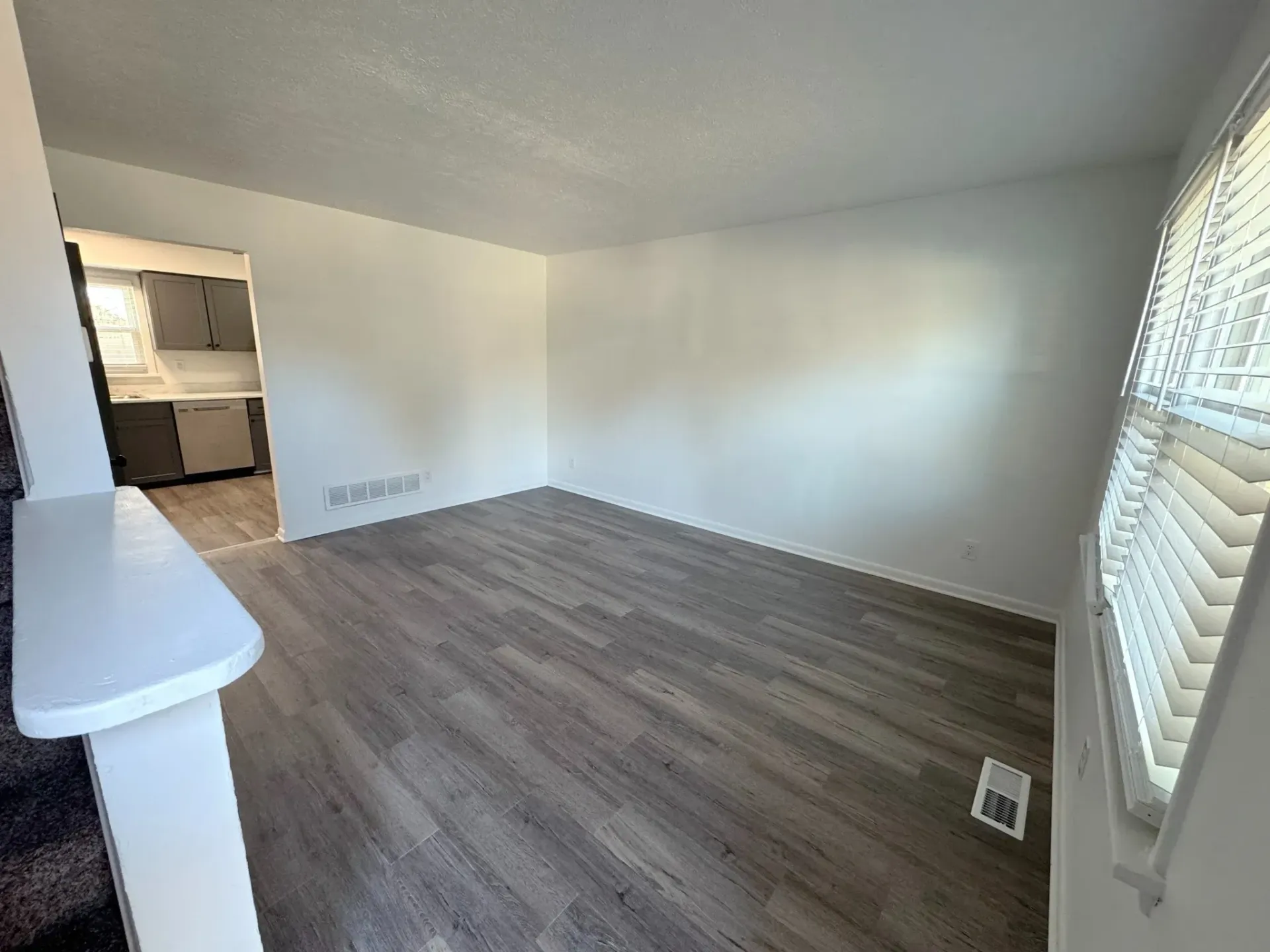 Empty living room with gray flooring, white walls, and a window with blinds.