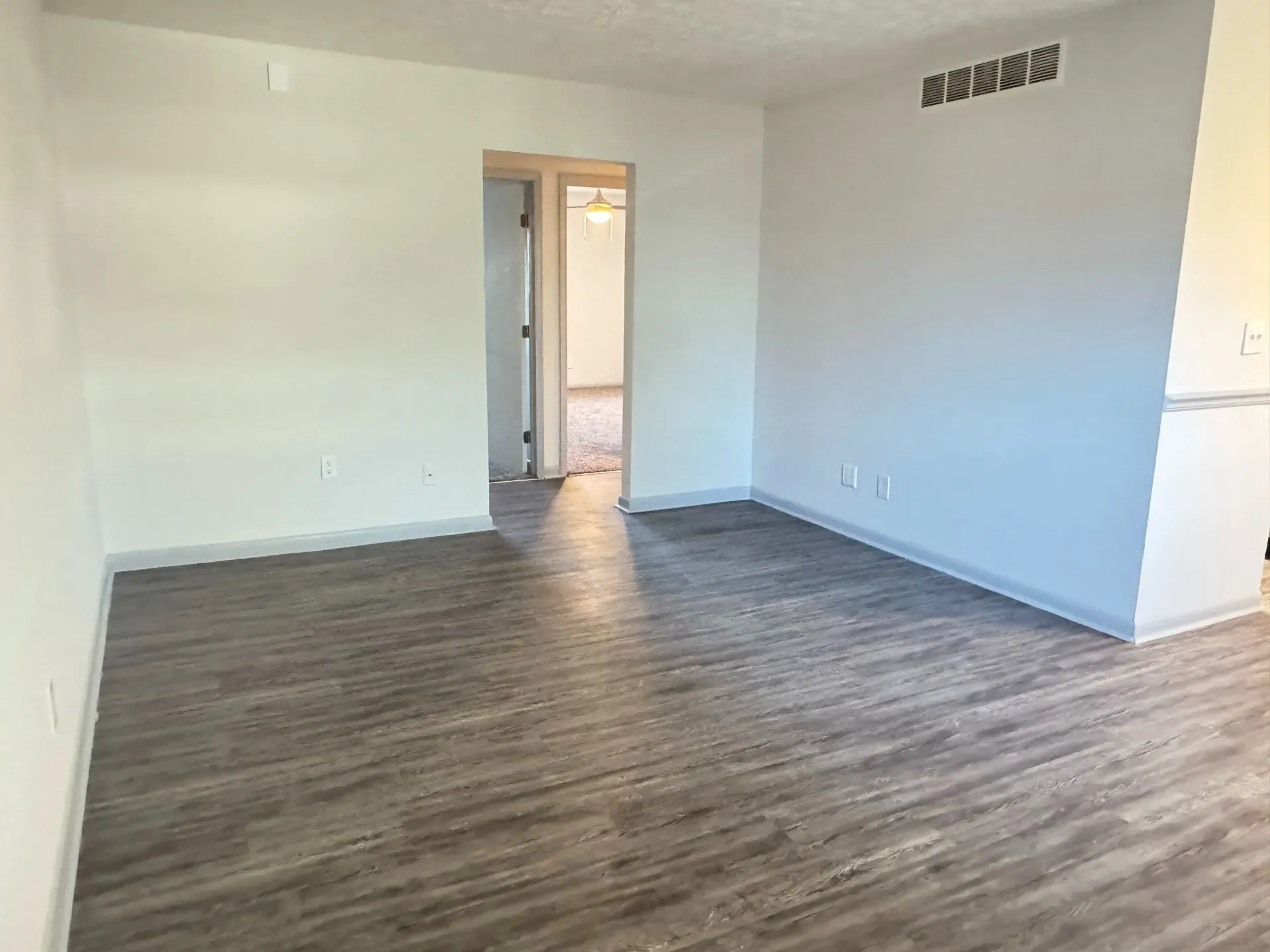 Empty living room with wood-look flooring, white walls, and doorway to another room.