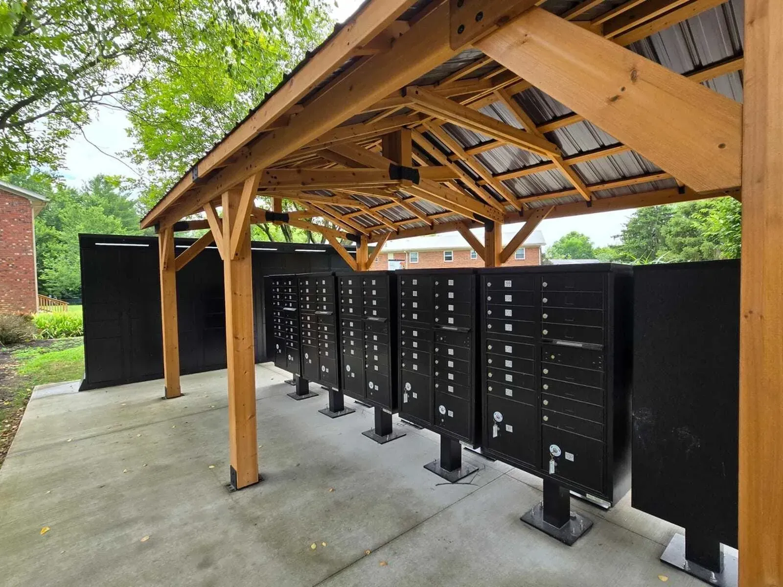 Mailboxes under a wooden roof, with black side panels, on a concrete pad.