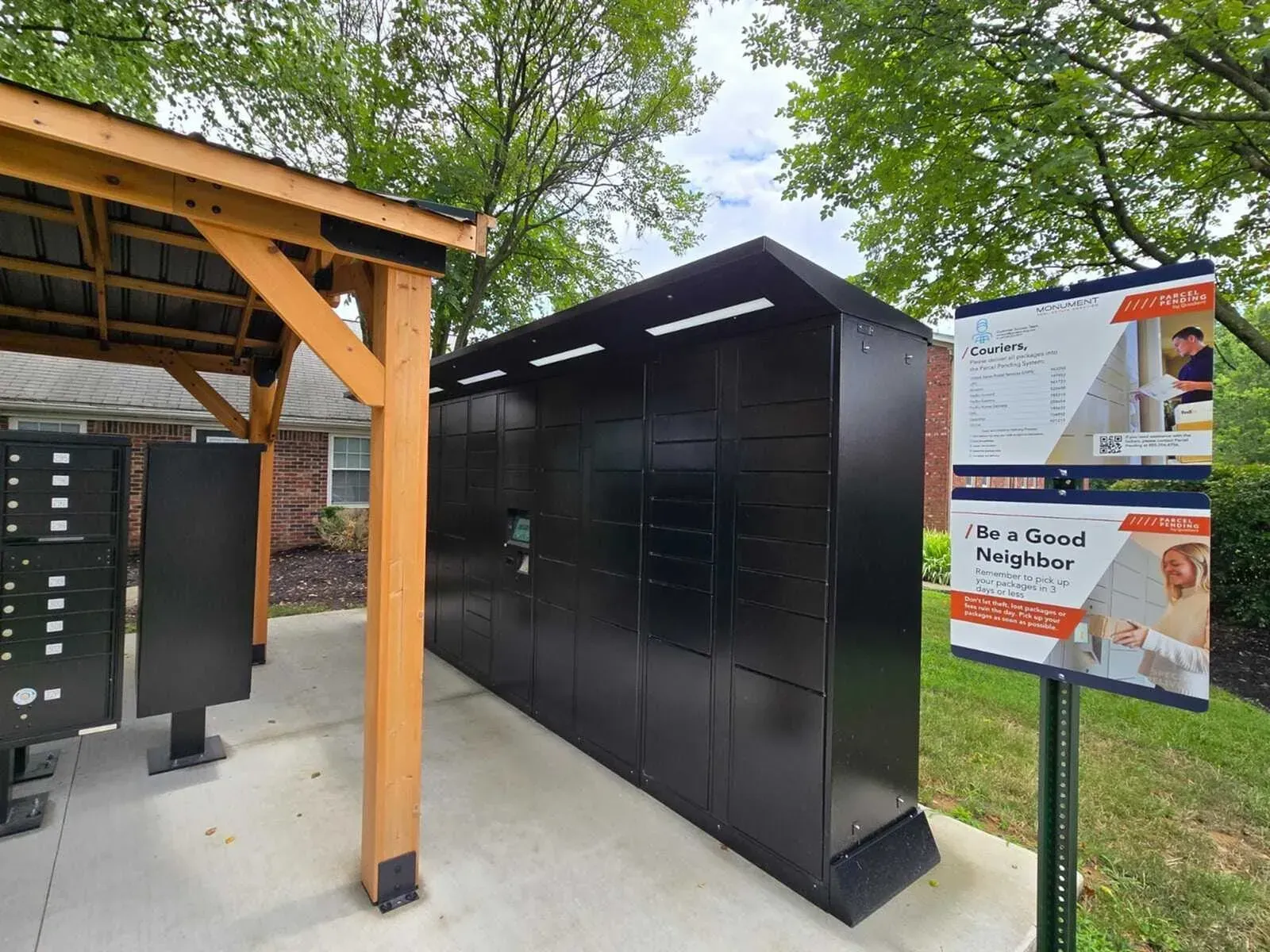 Black package lockers under a wooden shelter; sign to right.