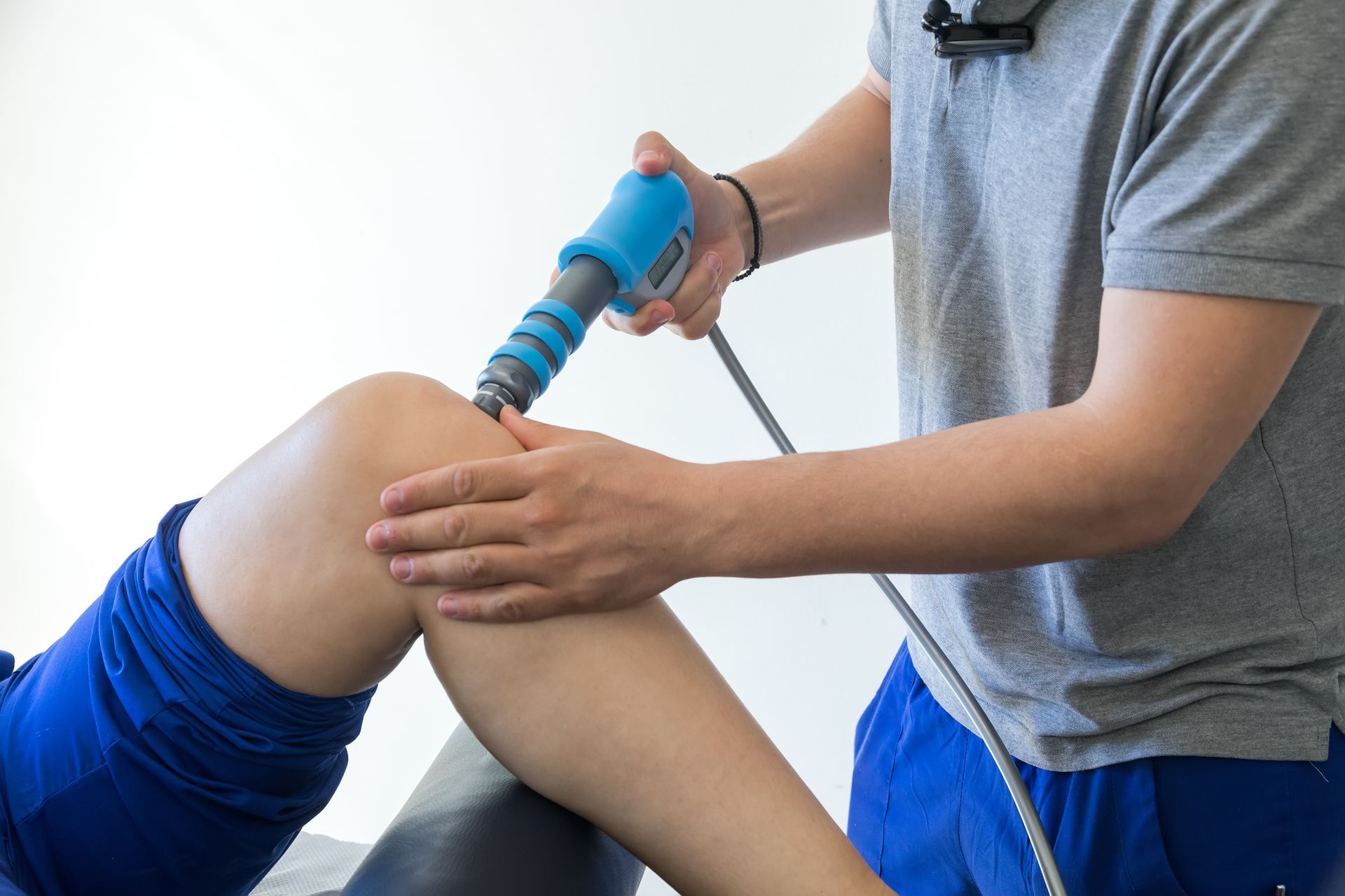 Therapist using a shockwave therapy device on a patient's knee.