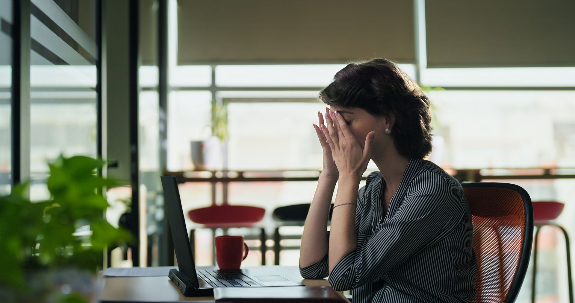 Woman holding her face in frustration at a desk with a laptop.