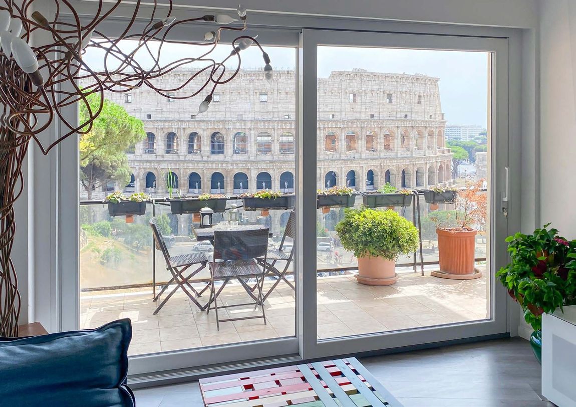 Le porte scorrevoli in vetro si aprono su un patio sul retro con divano, tavolo e un rigoglioso giardino verde.