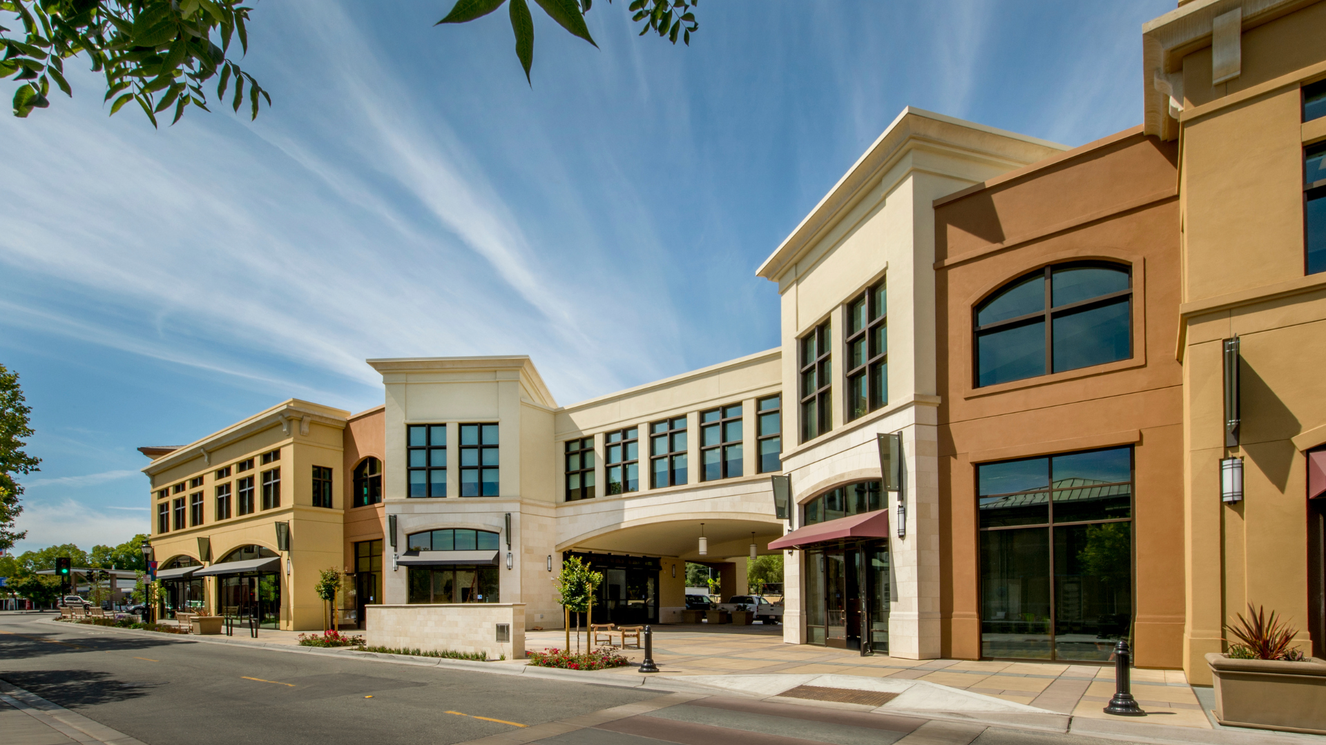 Row of modern beige storefronts along a sunny street with blue sky and wispy clouds