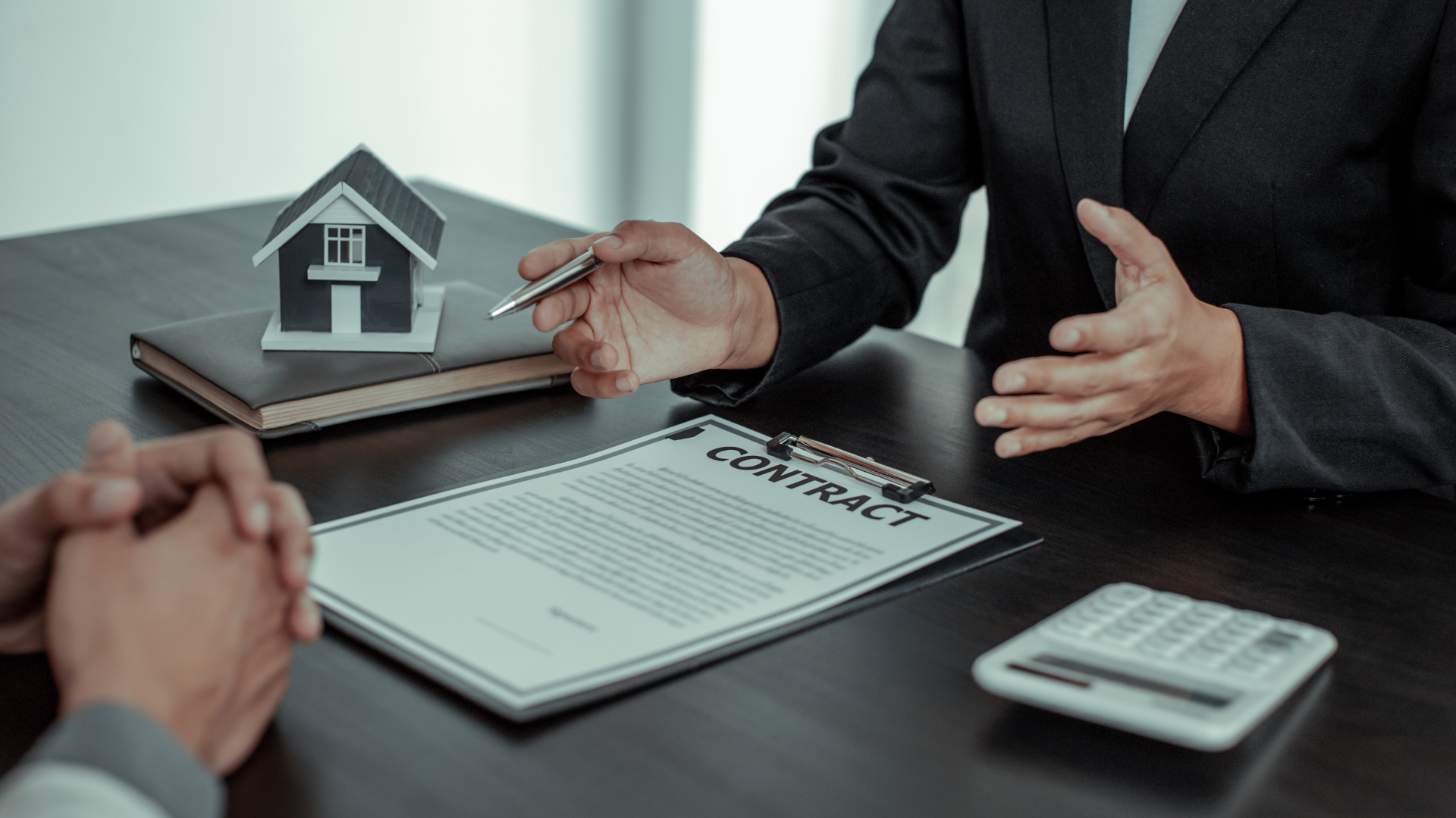 Business meeting with house model, paperwork, and calculator on a desk