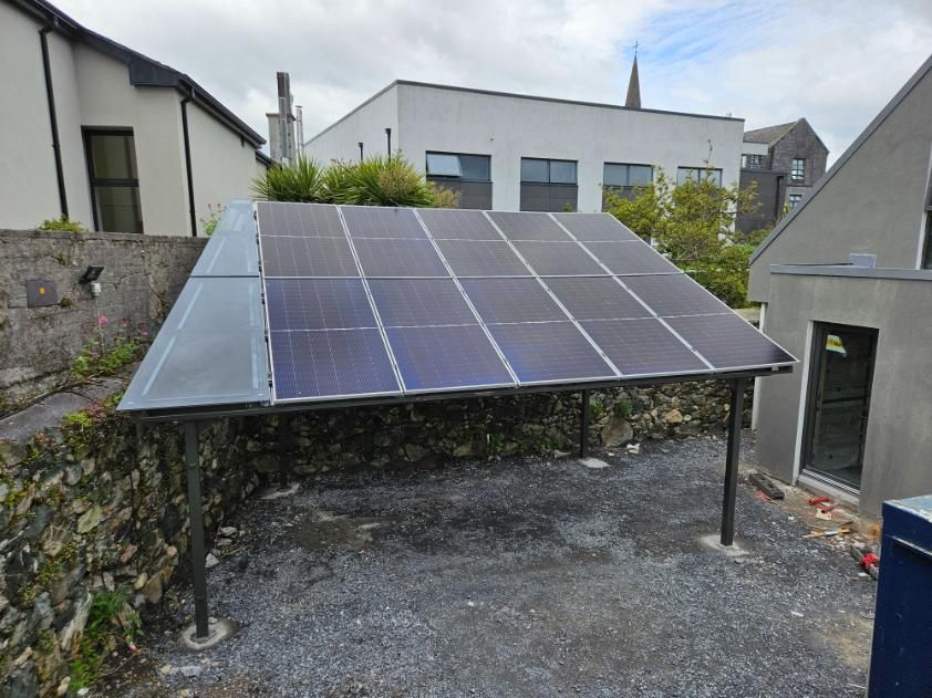 A row of solar panels are sitting under a canopy in front of a building.