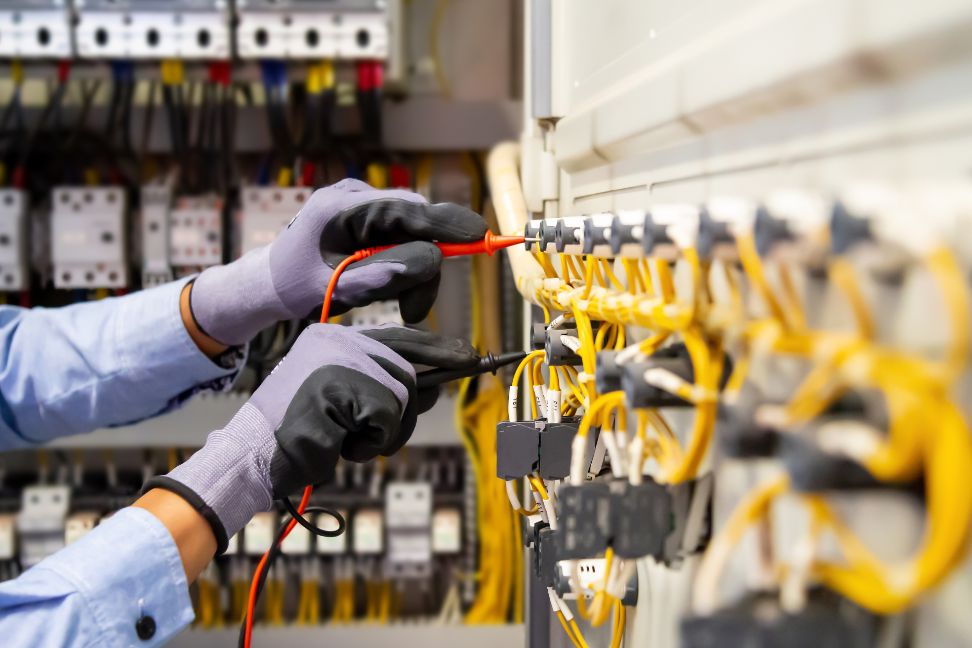 An electrician is working on an electrical panel with a voltage meter.