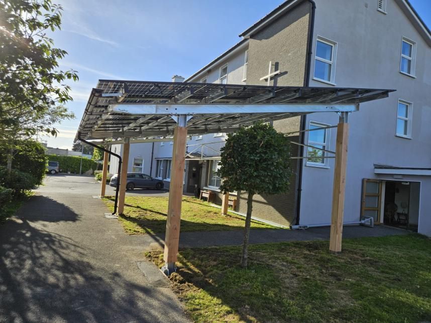 There is a carport with solar panels on it in front of a house.