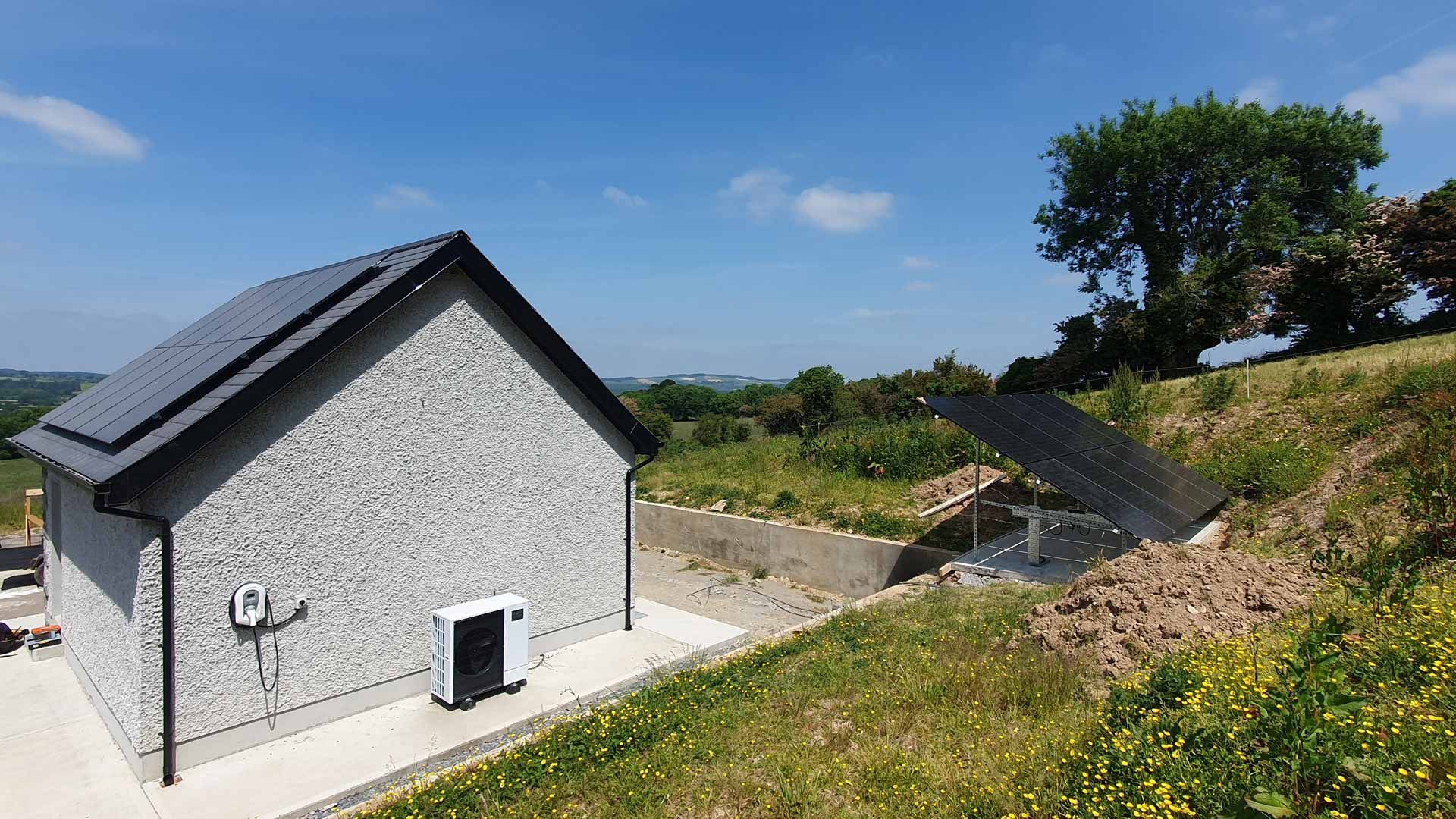 A small house with solar panels on the roof is sitting on top of a grassy hill.
