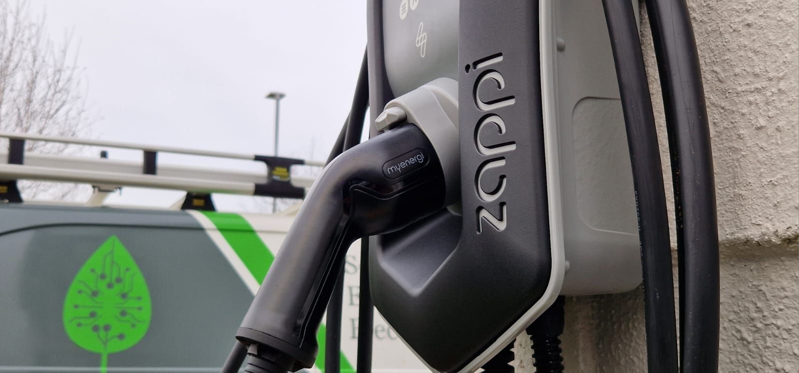 An electric car is being charged at a charging station on the side of a building.