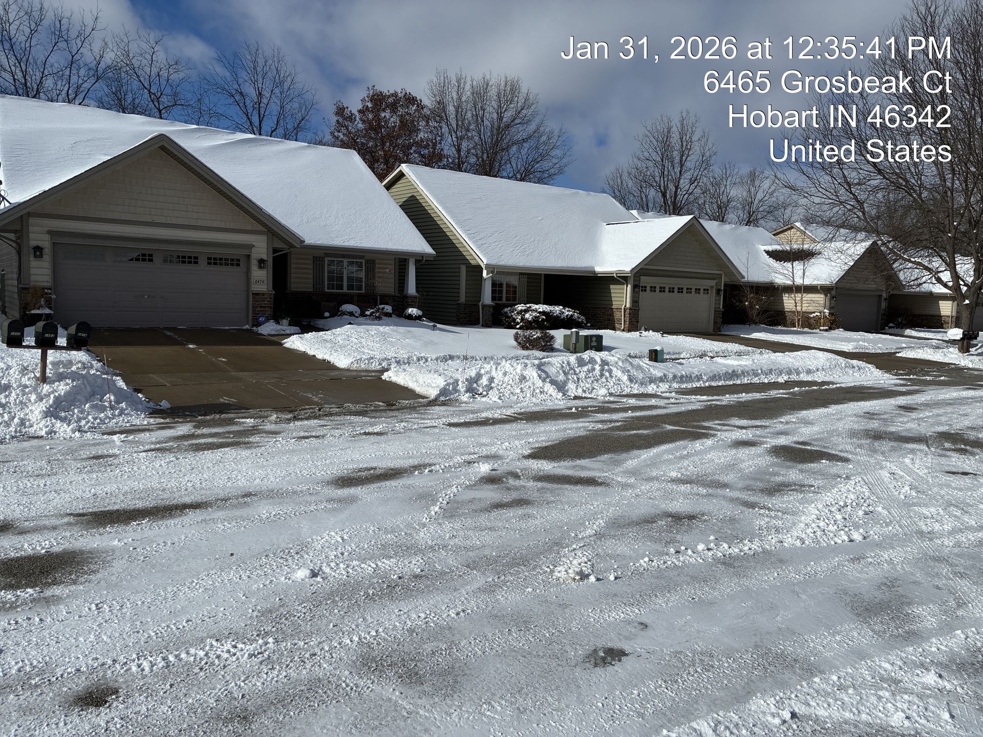 Snow-covered residential street with houses, garages, and clear blue sky on a sunny winter day