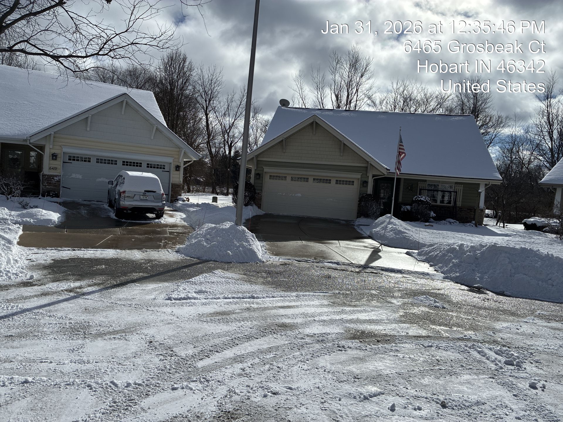 Snow-covered suburban street with two houses, parked cars, and a clear winter sky