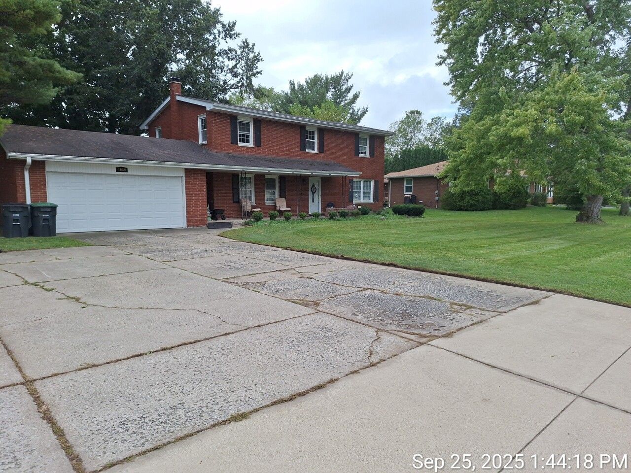 Suburban two-story brick house with attached garage, driveway, and large front lawn under cloudy skies