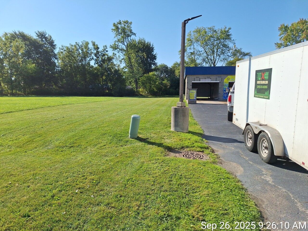 Grassy field beside a paved path, with a white truck and blue building under a clear sky