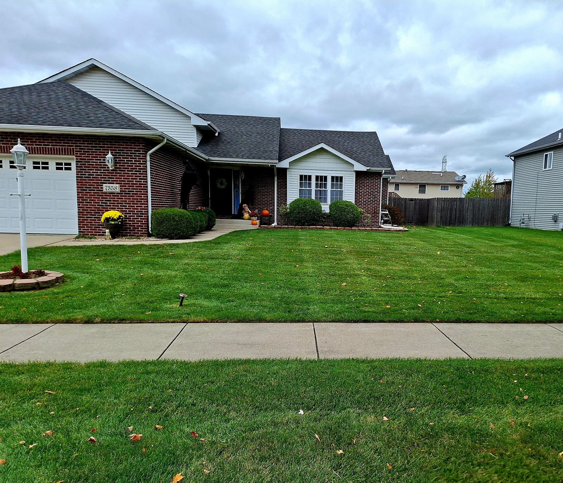Suburban brick house with manicured lawn, cloudy sky, and a white sign in the front yard