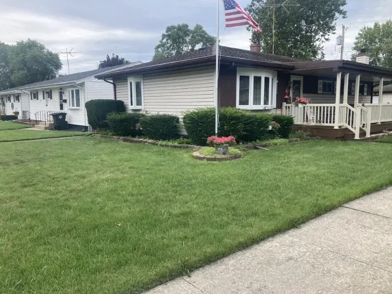 lawn maintenance hobart in Single-story white house with a porch, manicured lawn, and an American flag by the roadside.