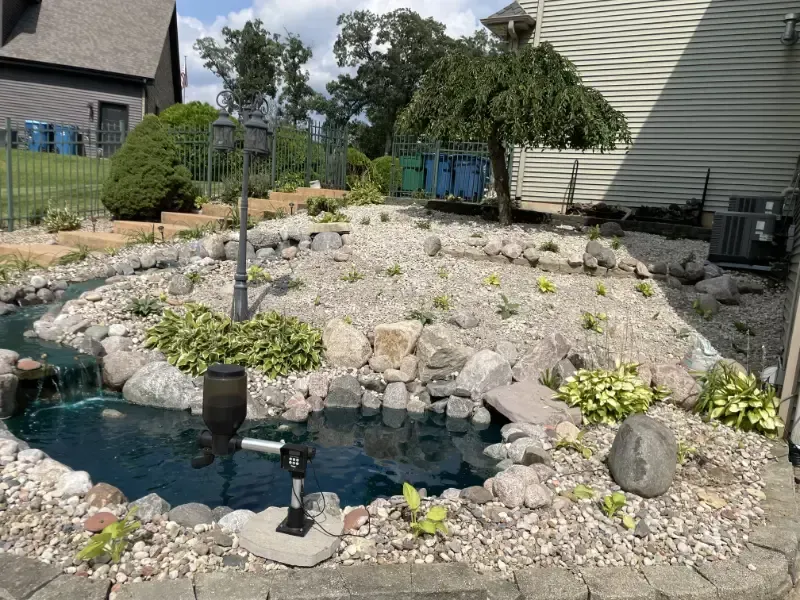 Backyard rock garden with a small pond, water feature, and low succulent plants beside a house