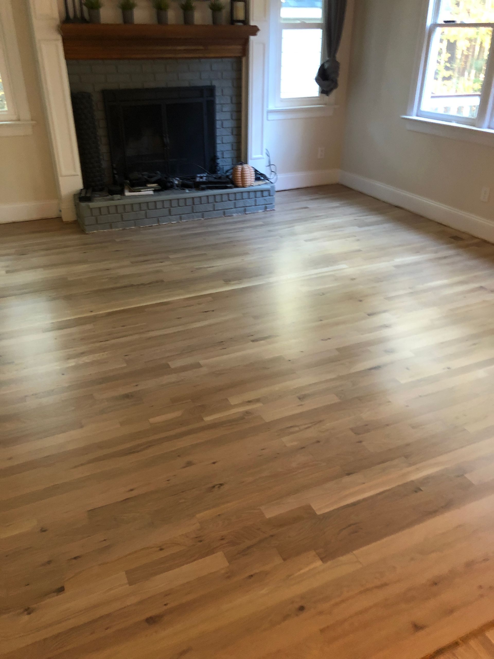 Light oak hardwood floor in a room, with a fireplace and windows.